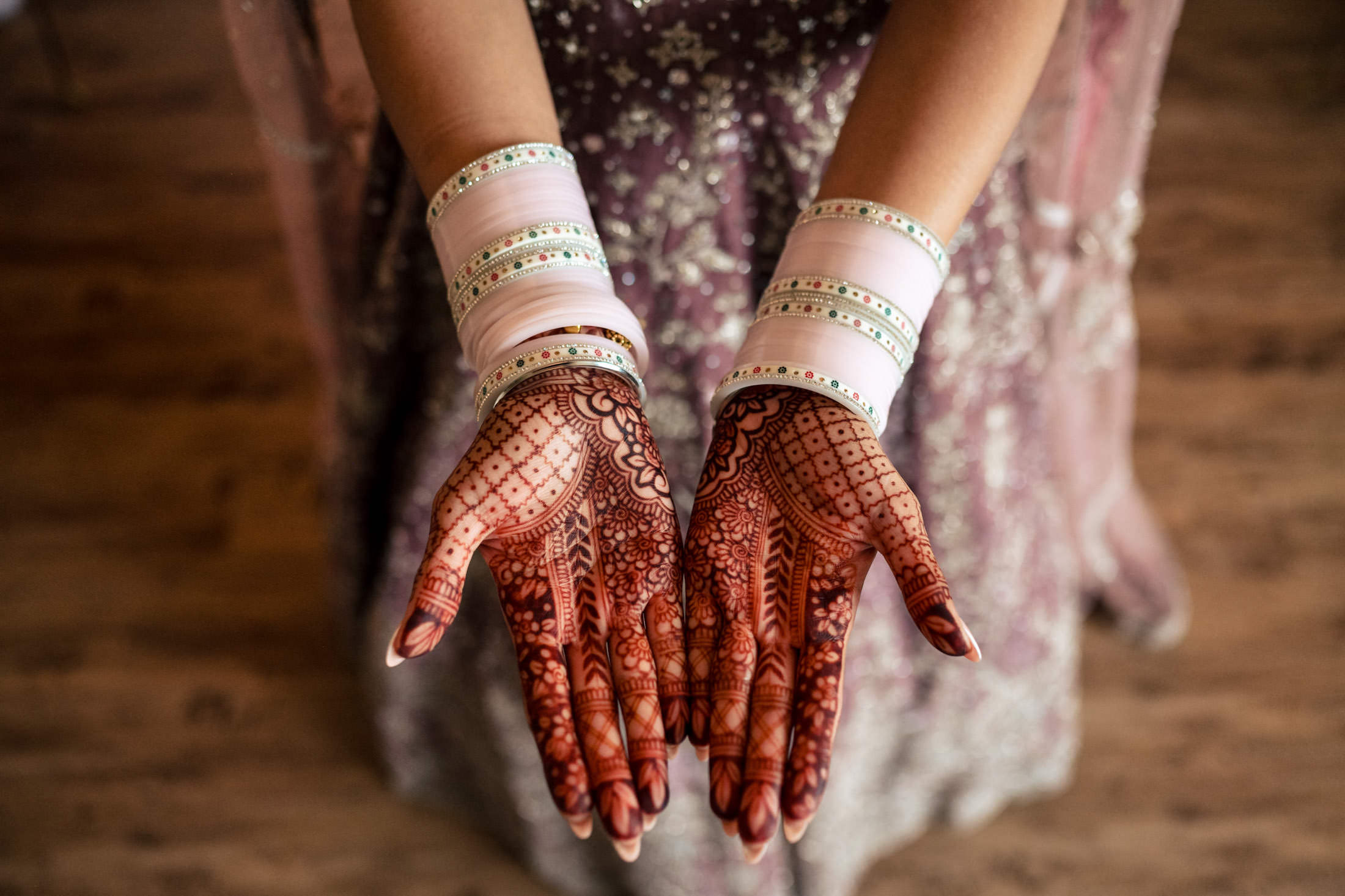 Open hands with henna and bangles, ready for a Winnipeg wedding, over a wooden floor.