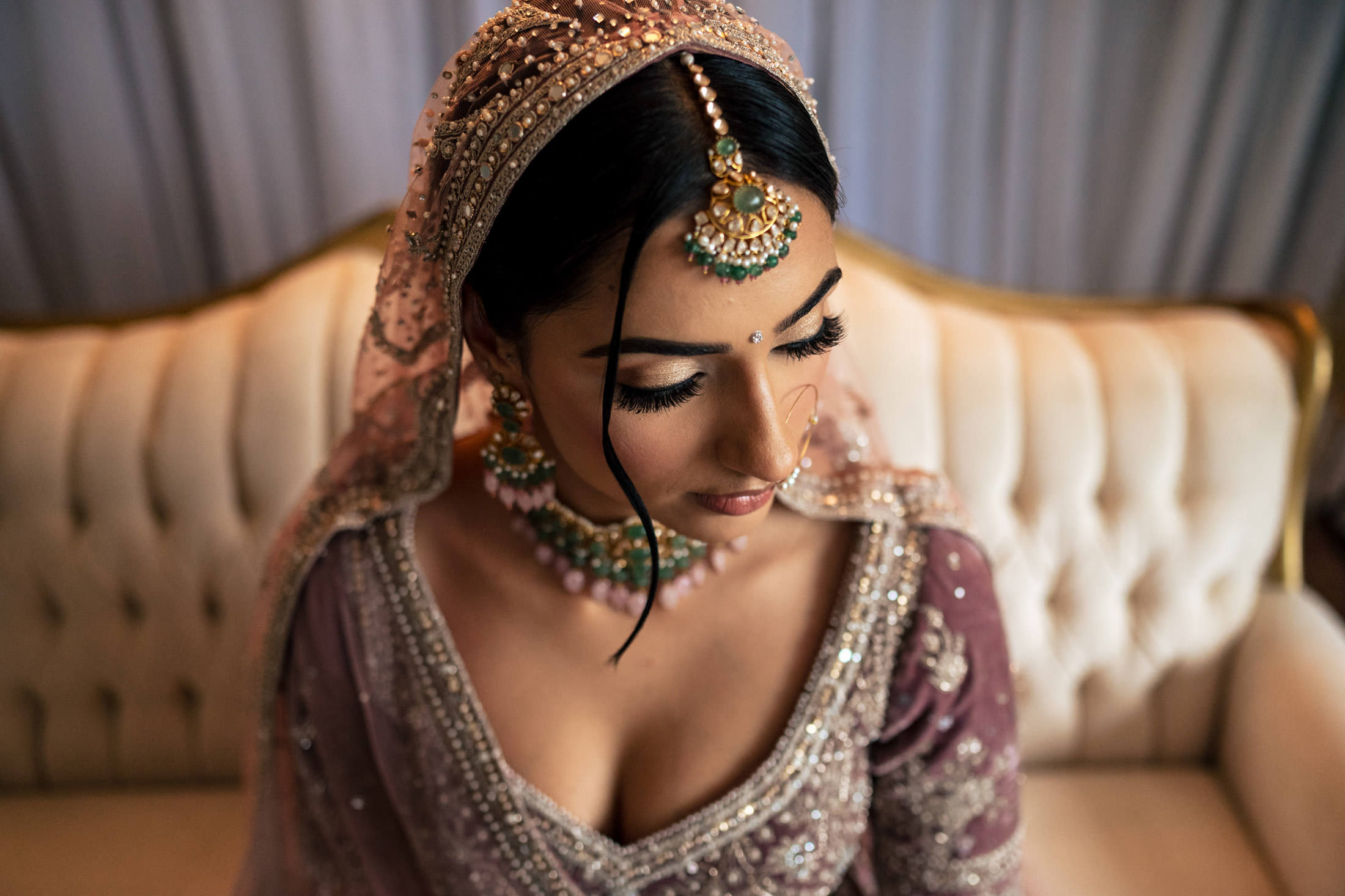Bride in ornate attire with jewelry sits on a white couch, captured from above at Winnipeg wedding.