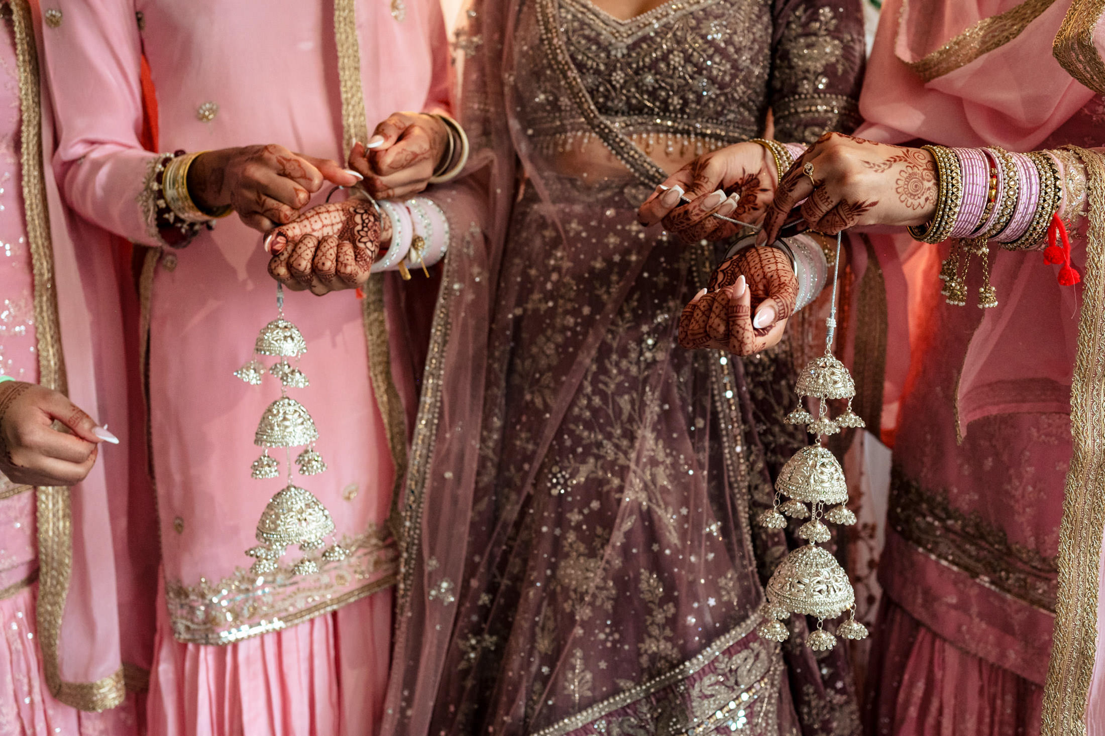 Women in ornate pink outfits and hennaed hands at a Winnipeg wedding with decorative tassels.