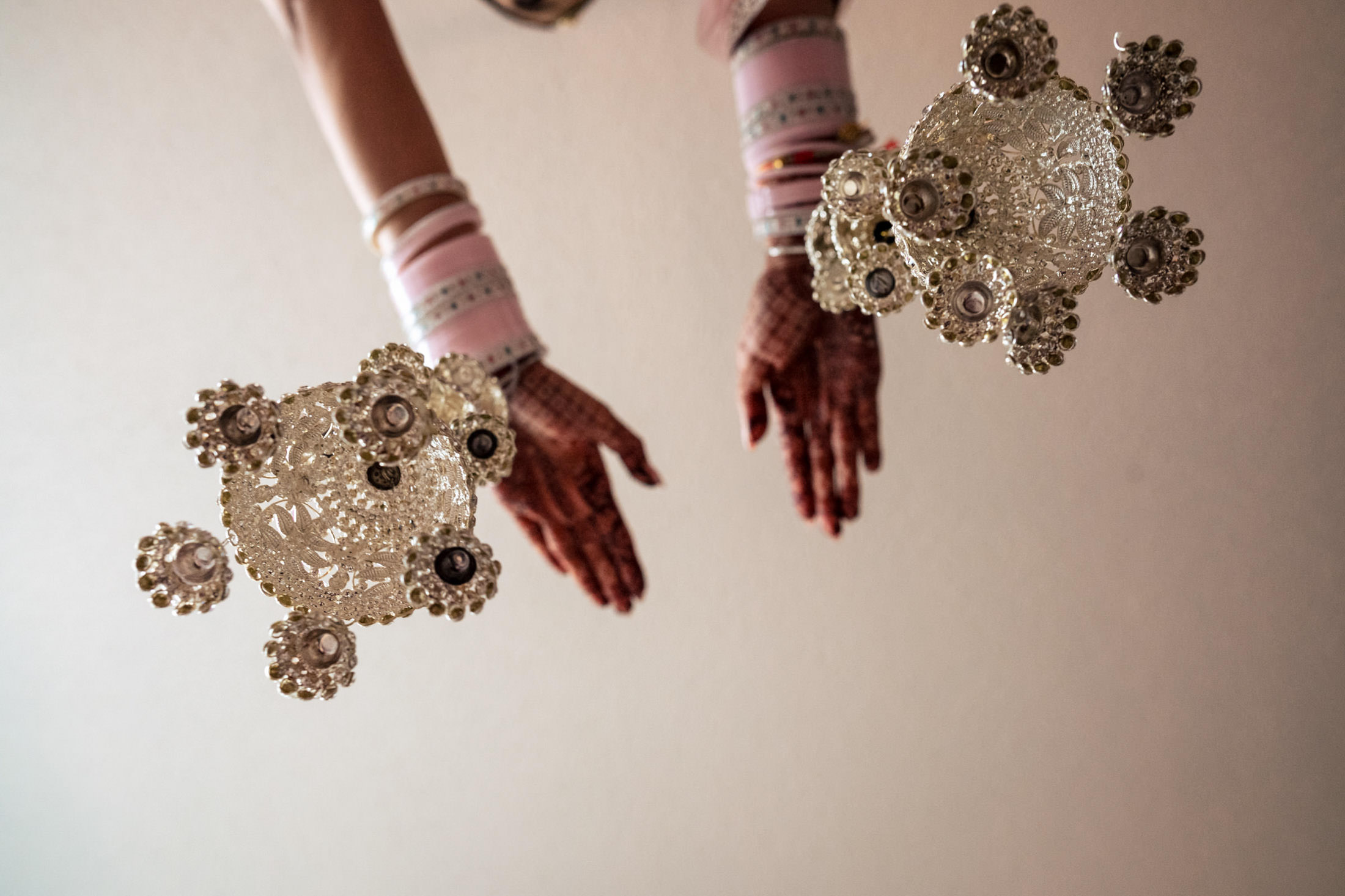 Henna-adorned hands cradle ornate silver at a Winnipeg wedding on a white backdrop.