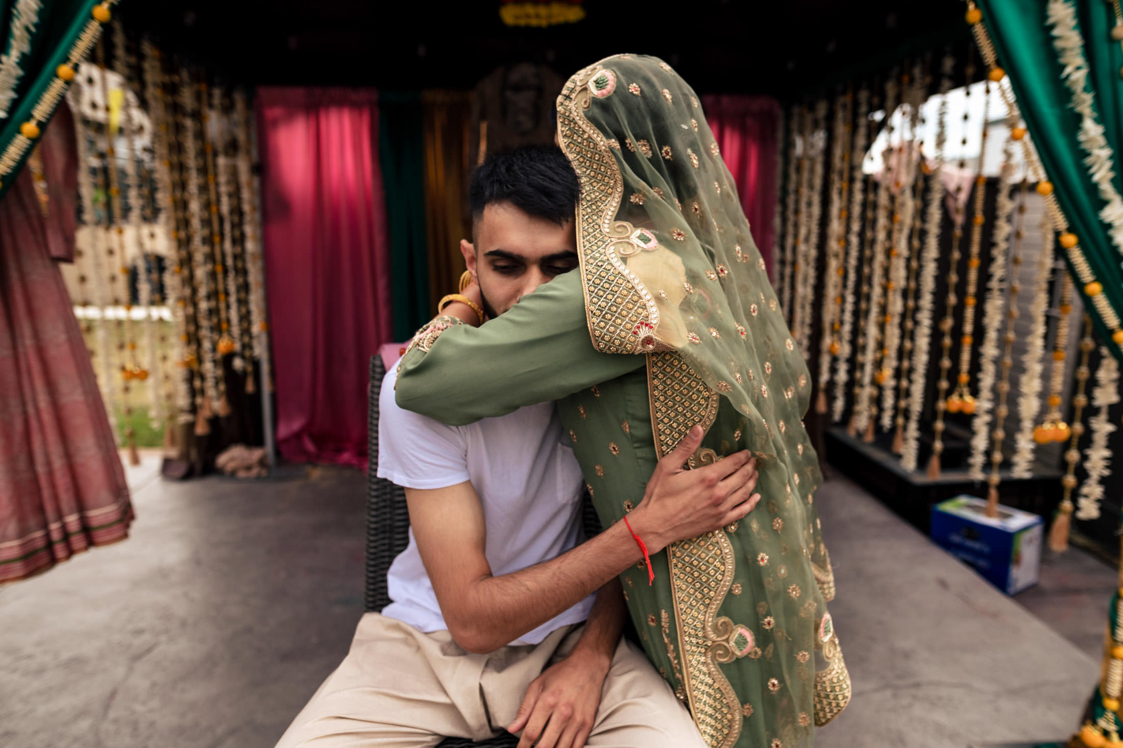 In green traditional attire, one hugs a seated person in white at a Winnipeg wedding.