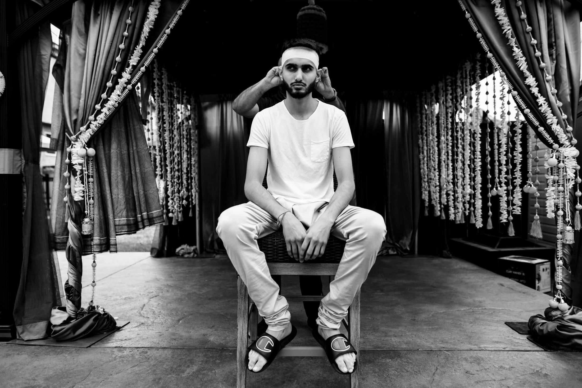 Person on stool, being adjusted by another, in a decorated space. Winnipeg wedding scene.