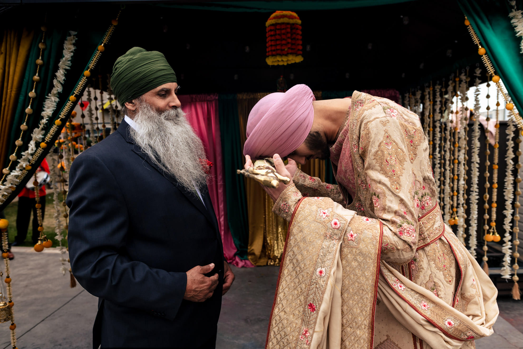 Two men in traditional attire, one bowing, at a colorful Winnipeg wedding.
