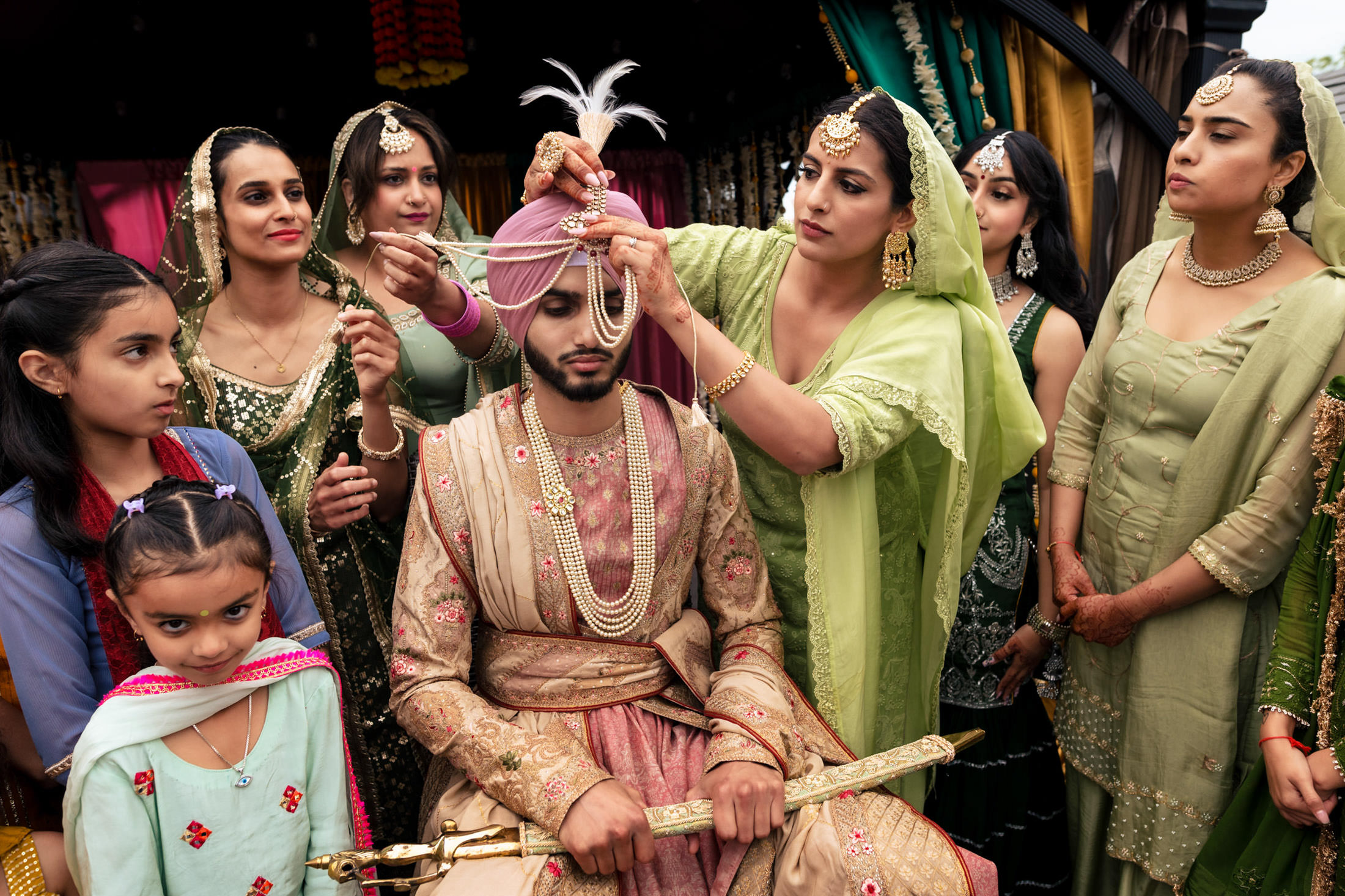 Groom in traditional attire at a Winnipeg wedding, women adjusting his turban and jewelry.
