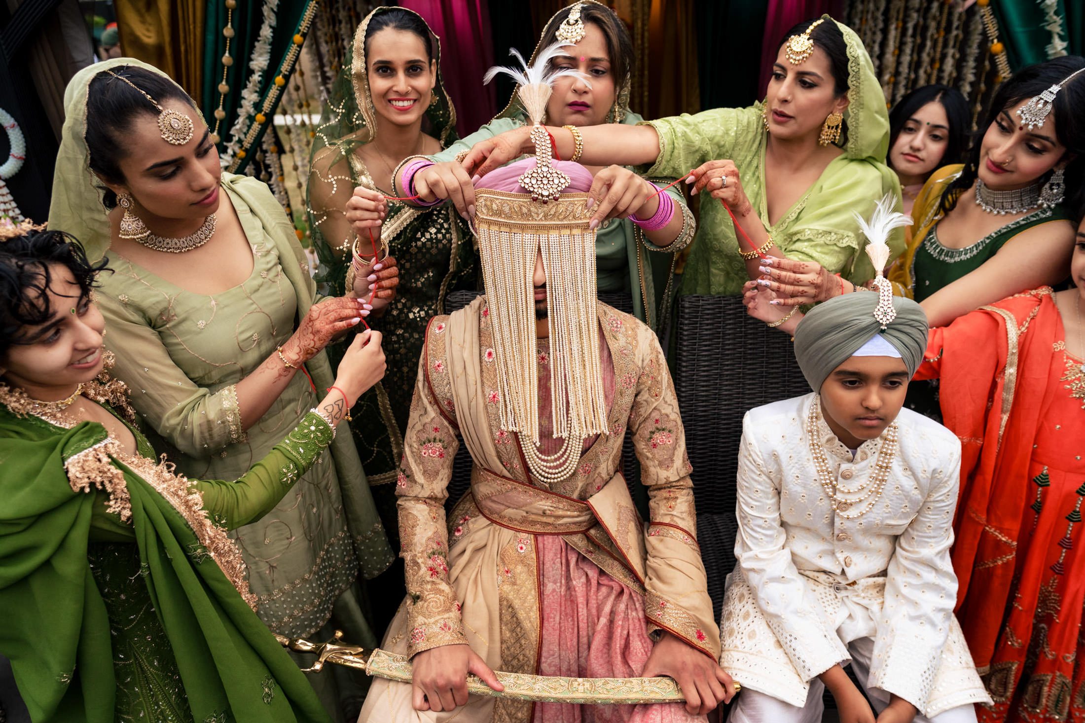 Groom with hidden face surrounded at a vibrant Winnipeg wedding by smiling, traditionally dressed friends.