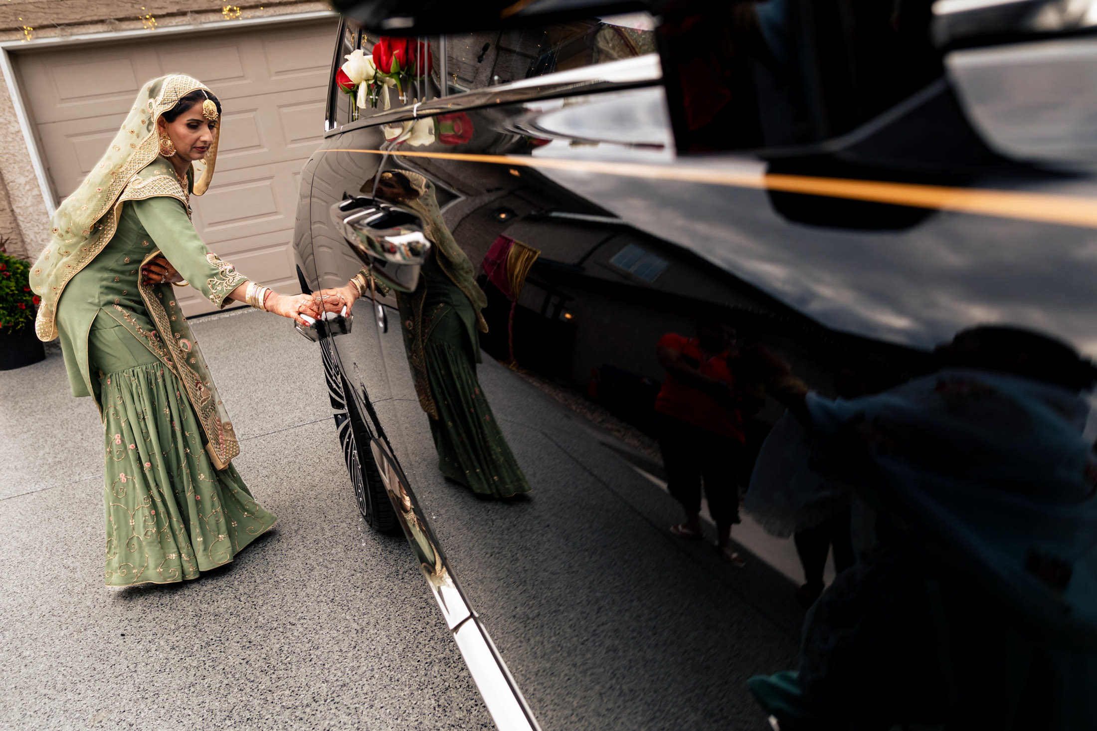 Bride in green dress reflected on car, opening door at Winnipeg wedding.