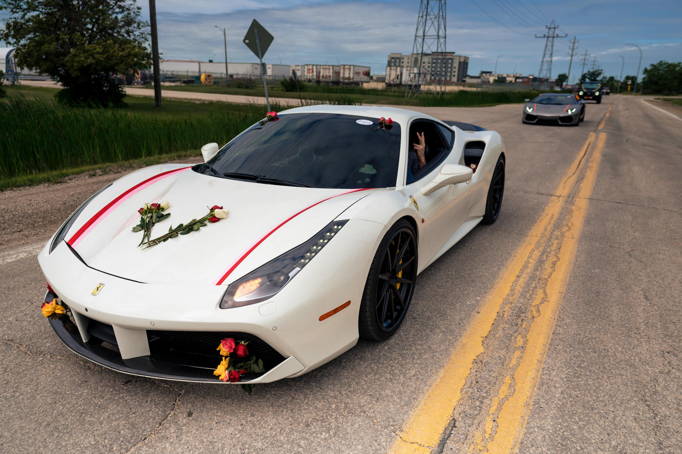 White sports car adorned with roses leads a Winnipeg wedding procession on the road.