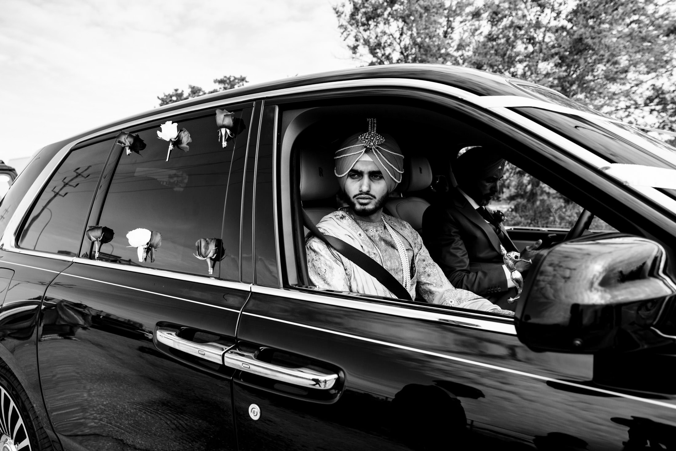 Man in traditional attire driving a decorated car at a Winnipeg wedding in monochrome.