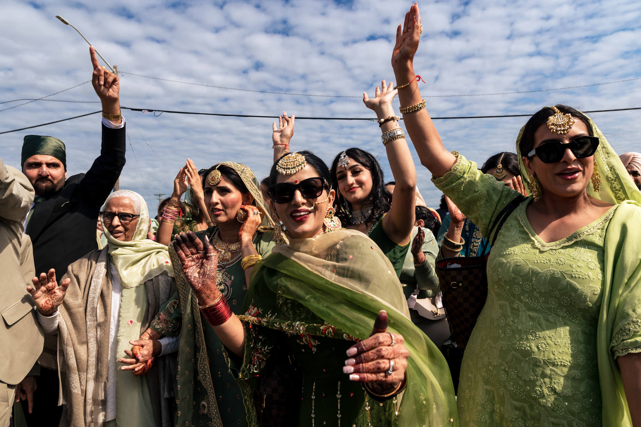 A group in traditional attire joyfully raises hands under Winnipeg's blue sky.