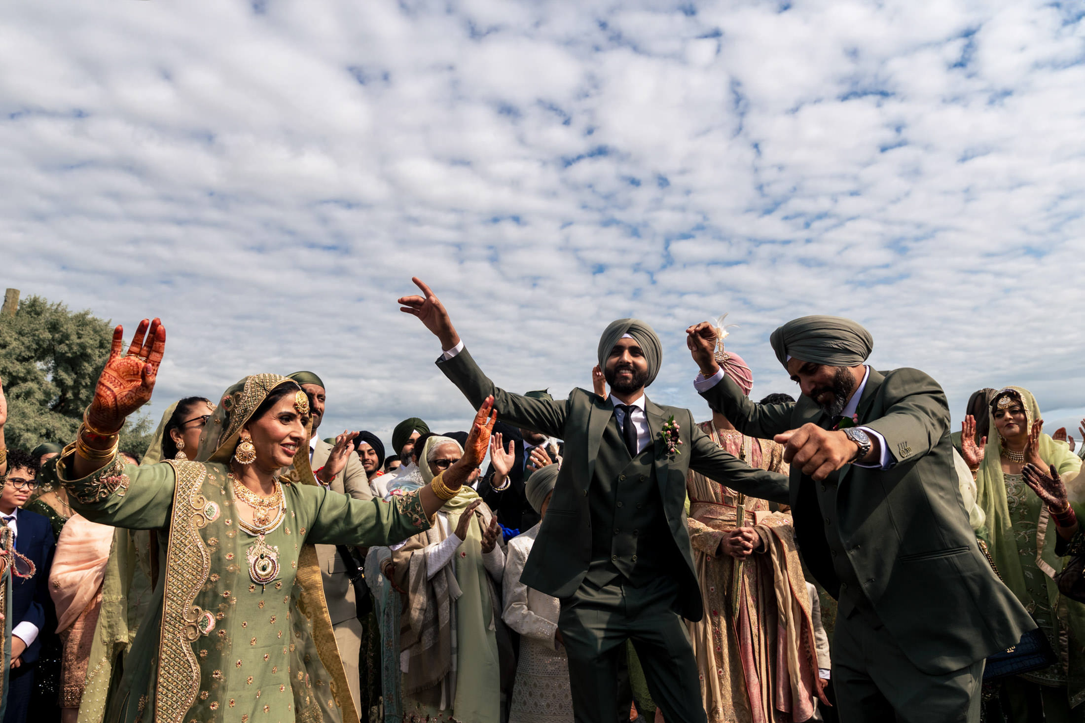 People in traditional attire joyfully dancing outdoors under a cloudy Winnipeg wedding sky.