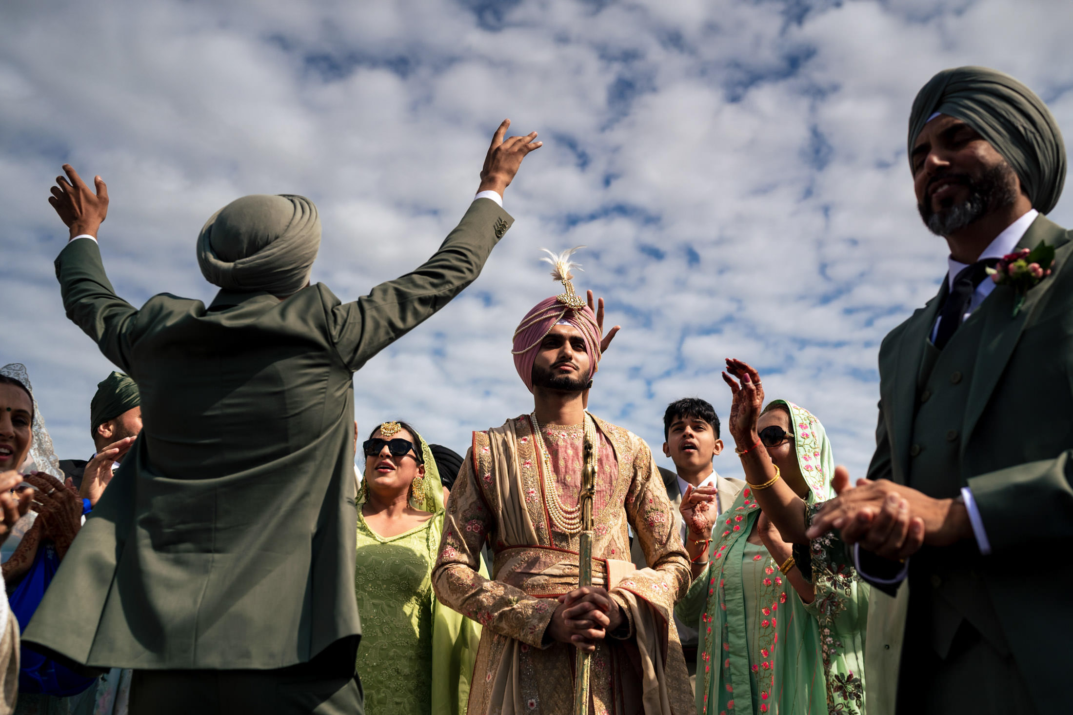 Winnipeg wedding guests in traditional attire celebrate outdoors beneath a cloudy sky.