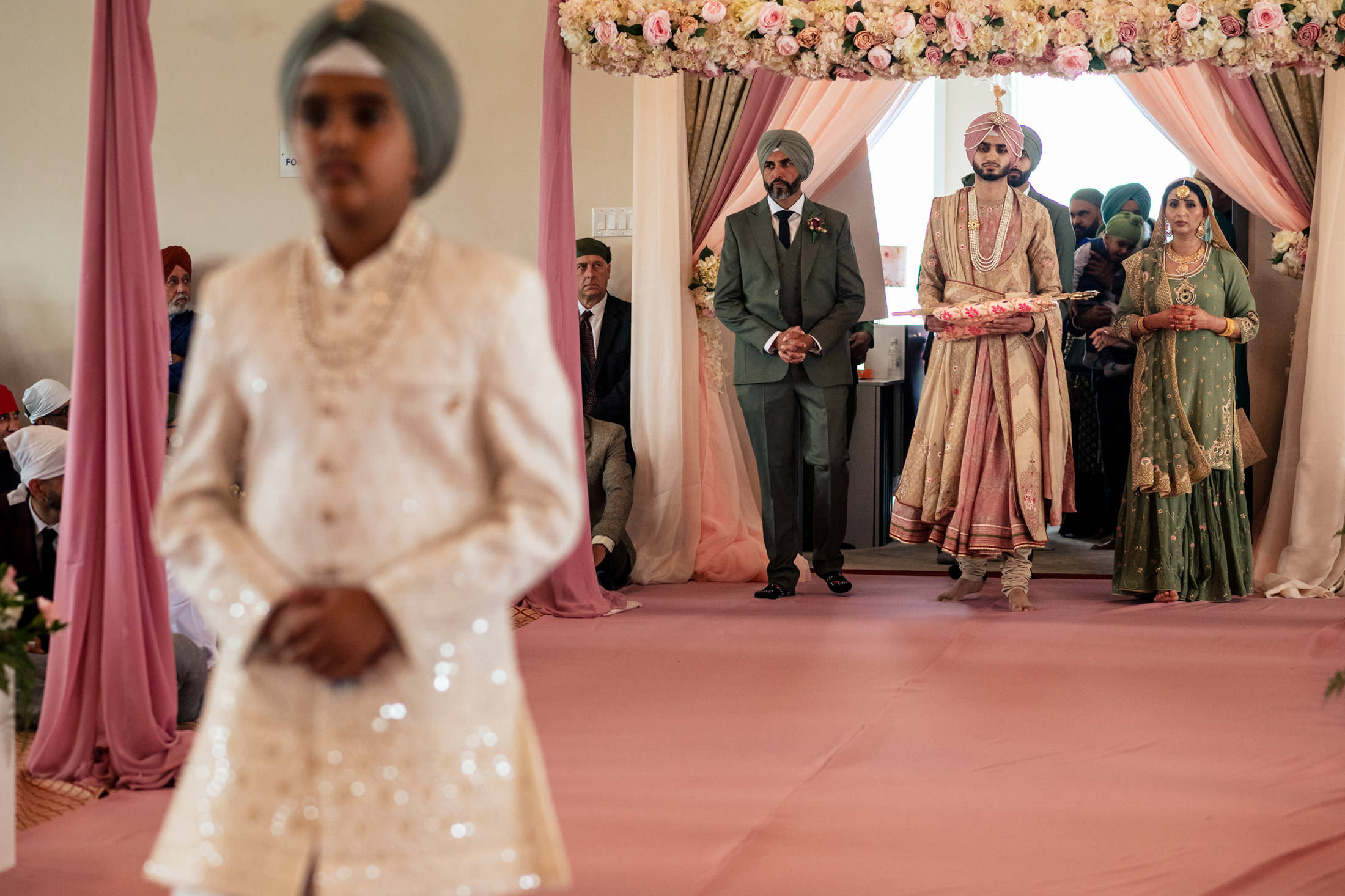 A groom and wedding party in traditional attire walk under a floral arch at a Winnipeg wedding.