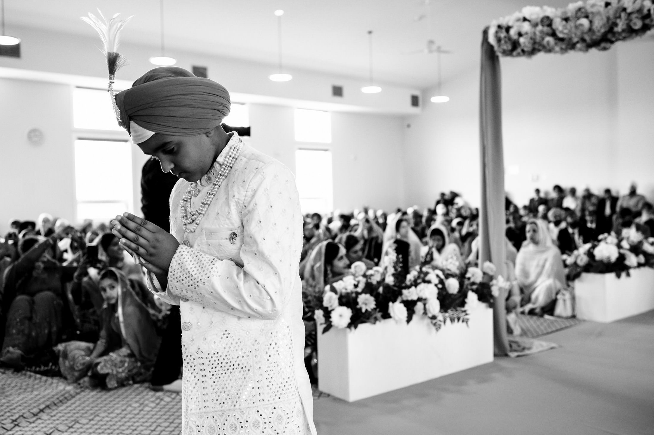 Boy in traditional attire prays at a large indoor Winnipeg wedding ceremony.