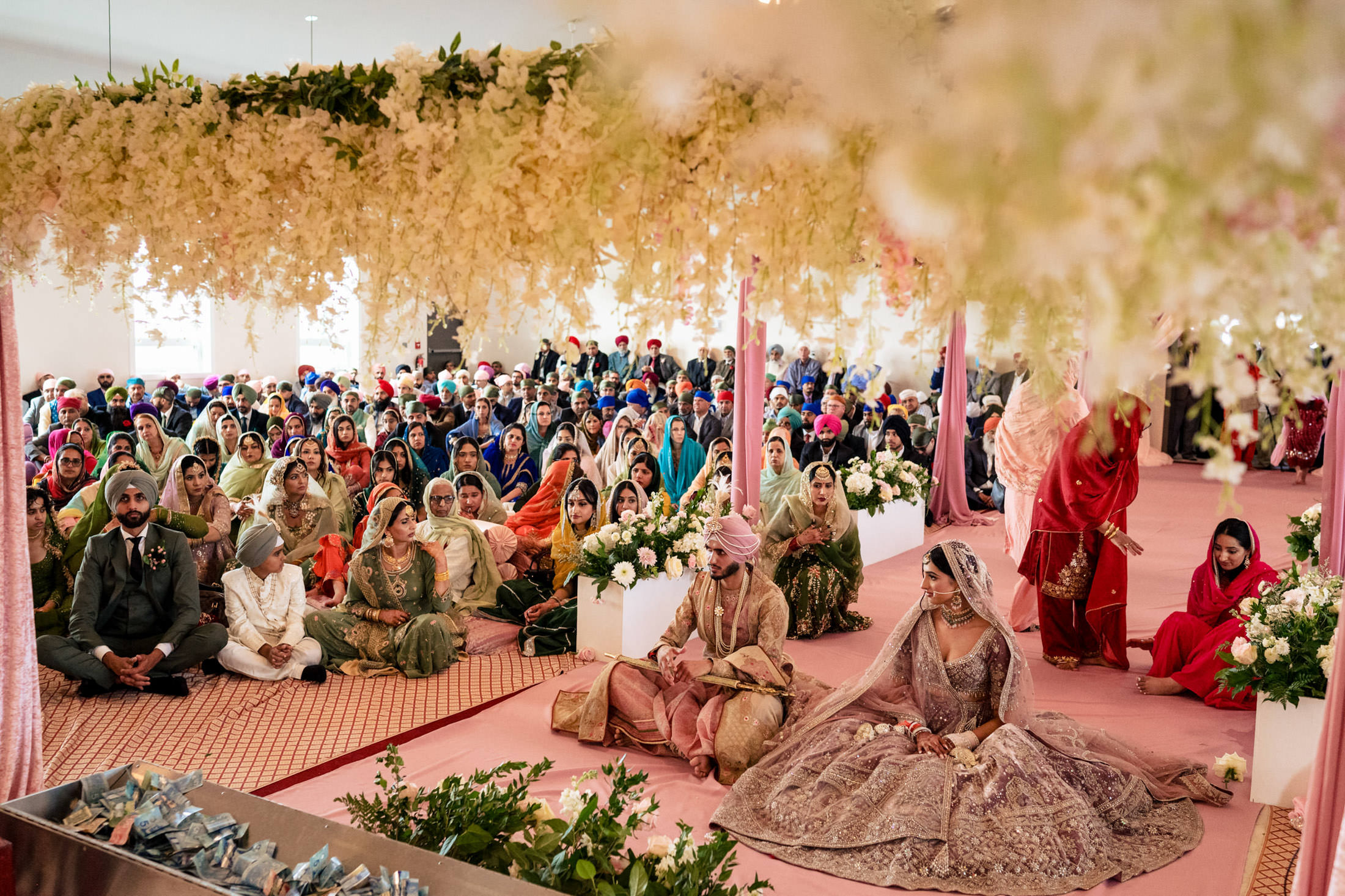 A couple sits at a colorful, floral Winnipeg wedding with a seated audience watching.
