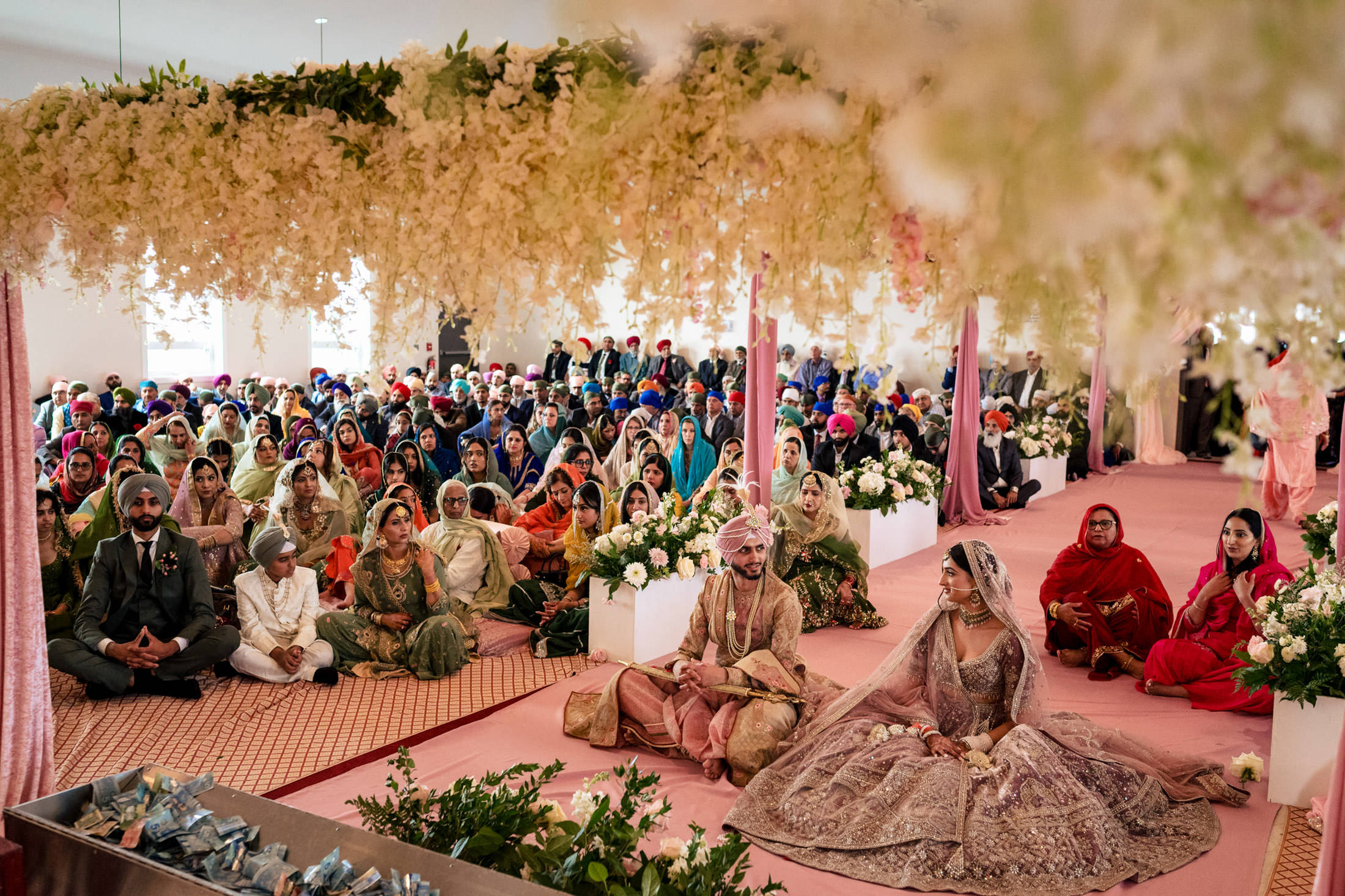A couple in traditional attire at a vibrant Winnipeg wedding with guests seated indoors.