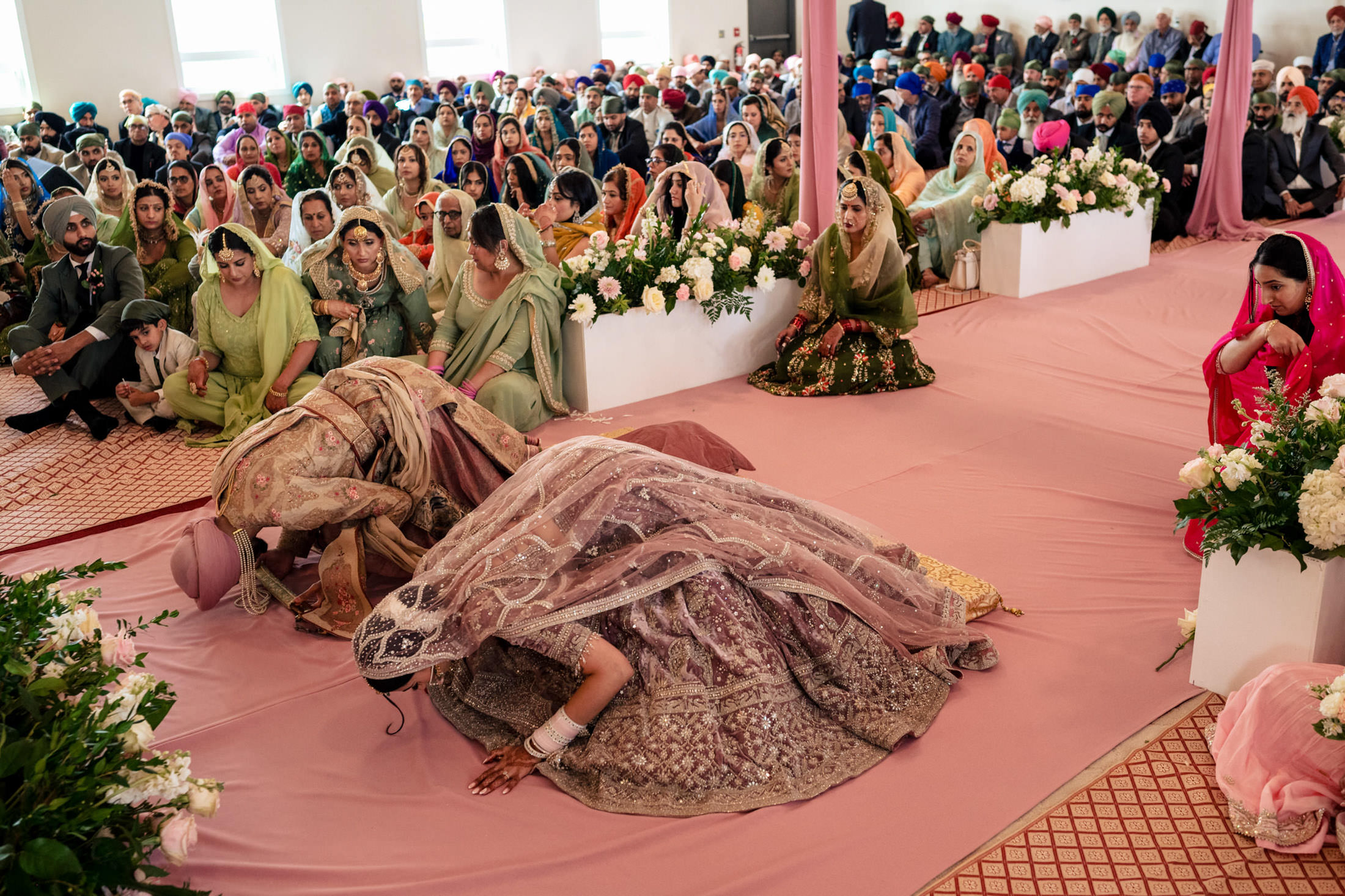 Couple in traditional attire bowing during a Winnipeg wedding with guests around.