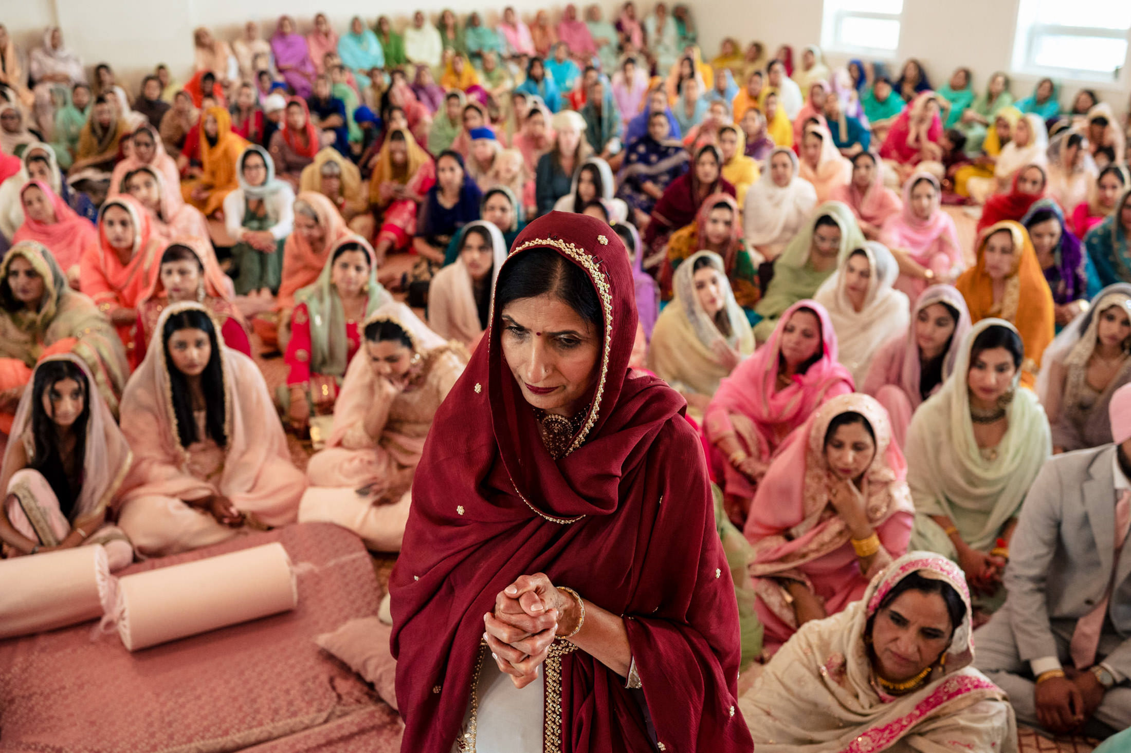 A woman in red prays at a seated group during a colorful Winnipeg wedding.