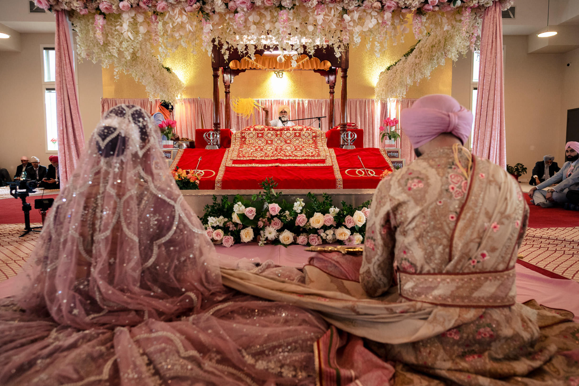 Bride and groom seated at a Sikh ceremony in Winnipeg, surrounded by flowers and decorations.