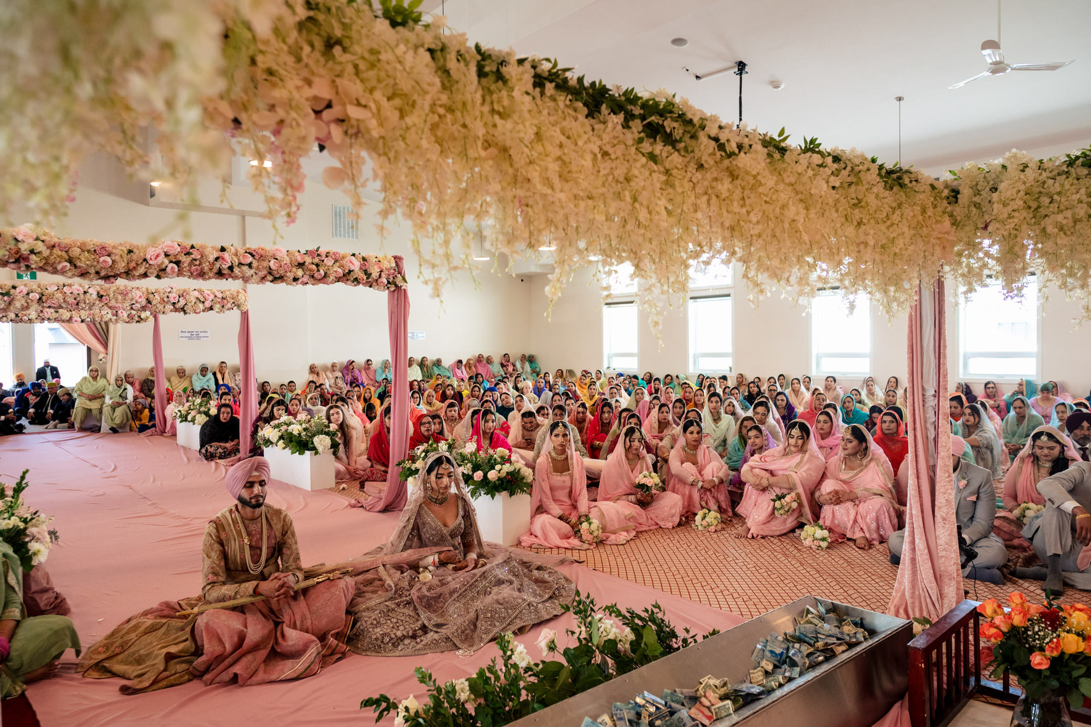 Colorful Winnipeg wedding with people seated under floral decorations in a bright hall.