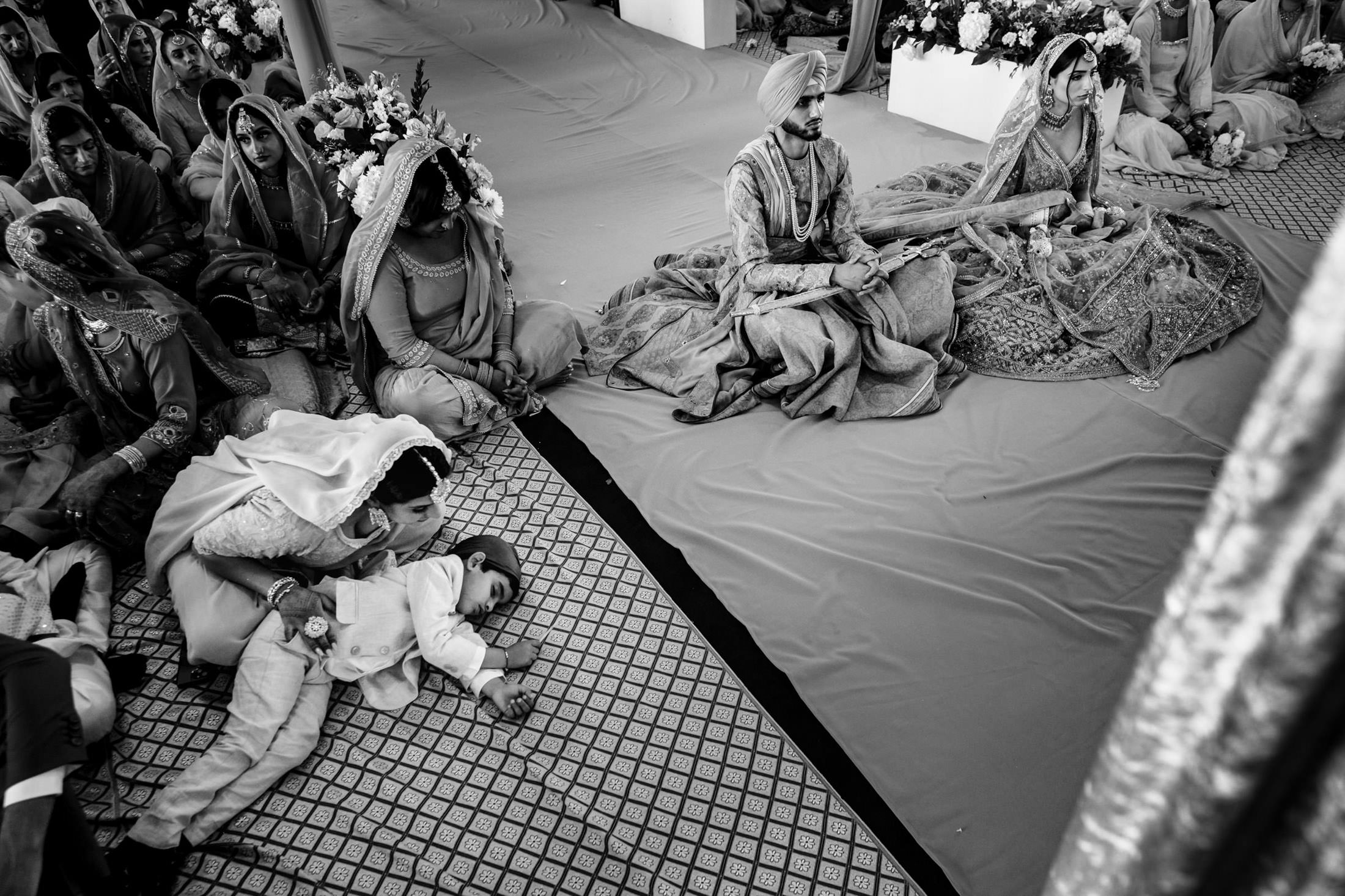 Winnipeg wedding: Sikh ceremony with couple seated, child nearby, and guests gathered around.