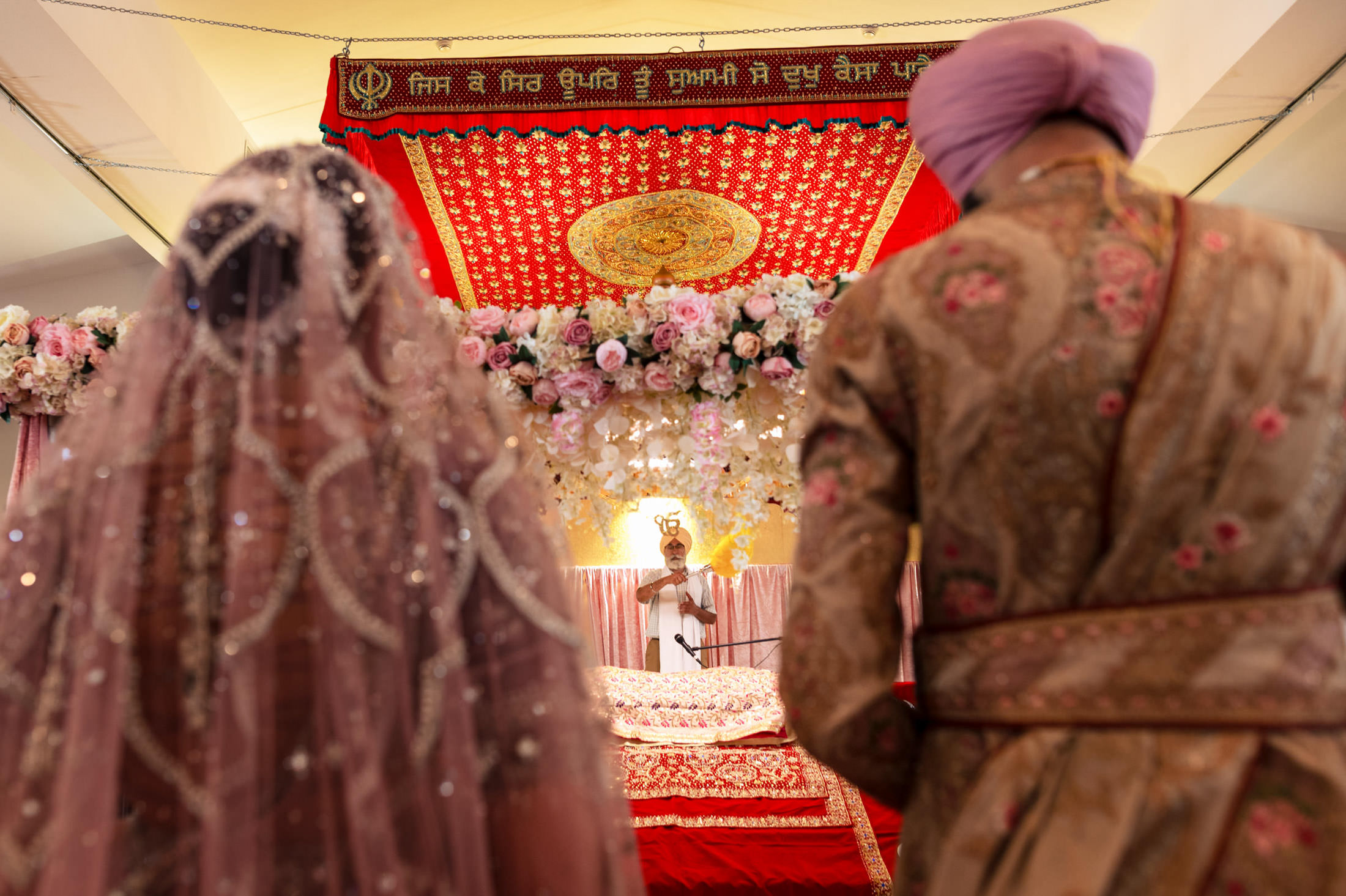 Sikh wedding ceremony in Winnipeg with couple in traditional attire under a floral canopy.