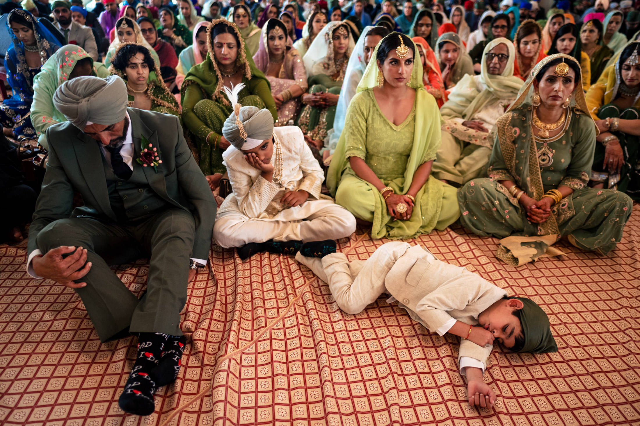 Guests in traditional attire sit on the floor at a vibrant Winnipeg wedding ceremony.