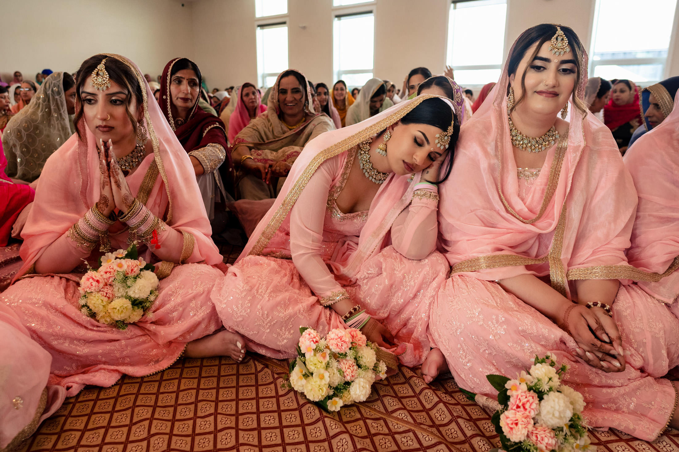 Three women in pink traditional attire at a Winnipeg wedding, sitting with bouquets.