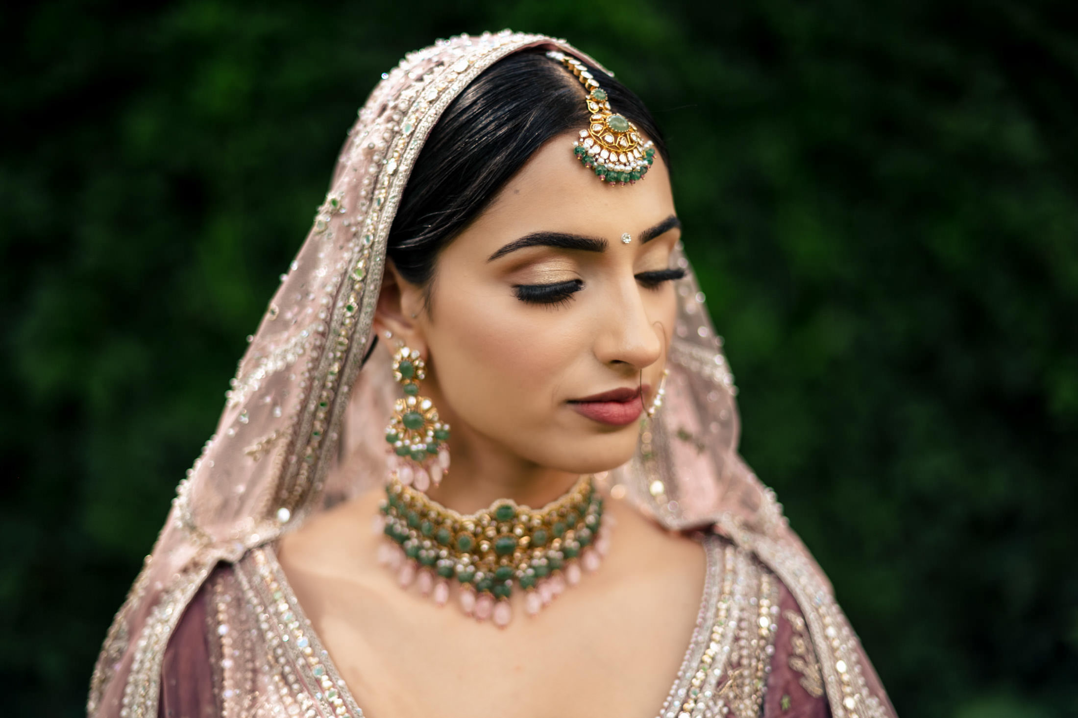 Bride in ornate traditional attire, eyes downcast, at a lush Winnipeg wedding.