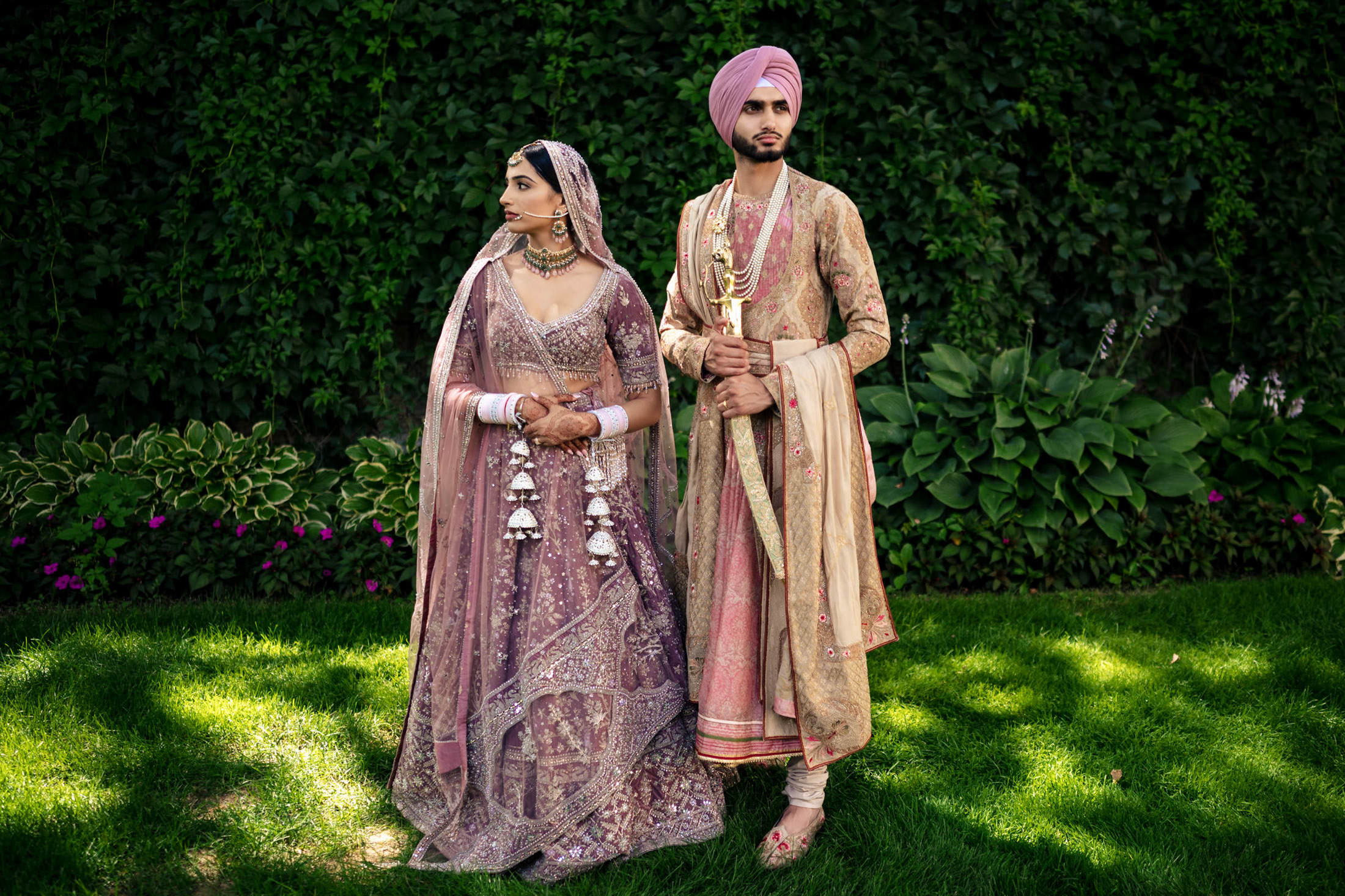 Couple in traditional attire at a Winnipeg wedding on green grass with leafy background.