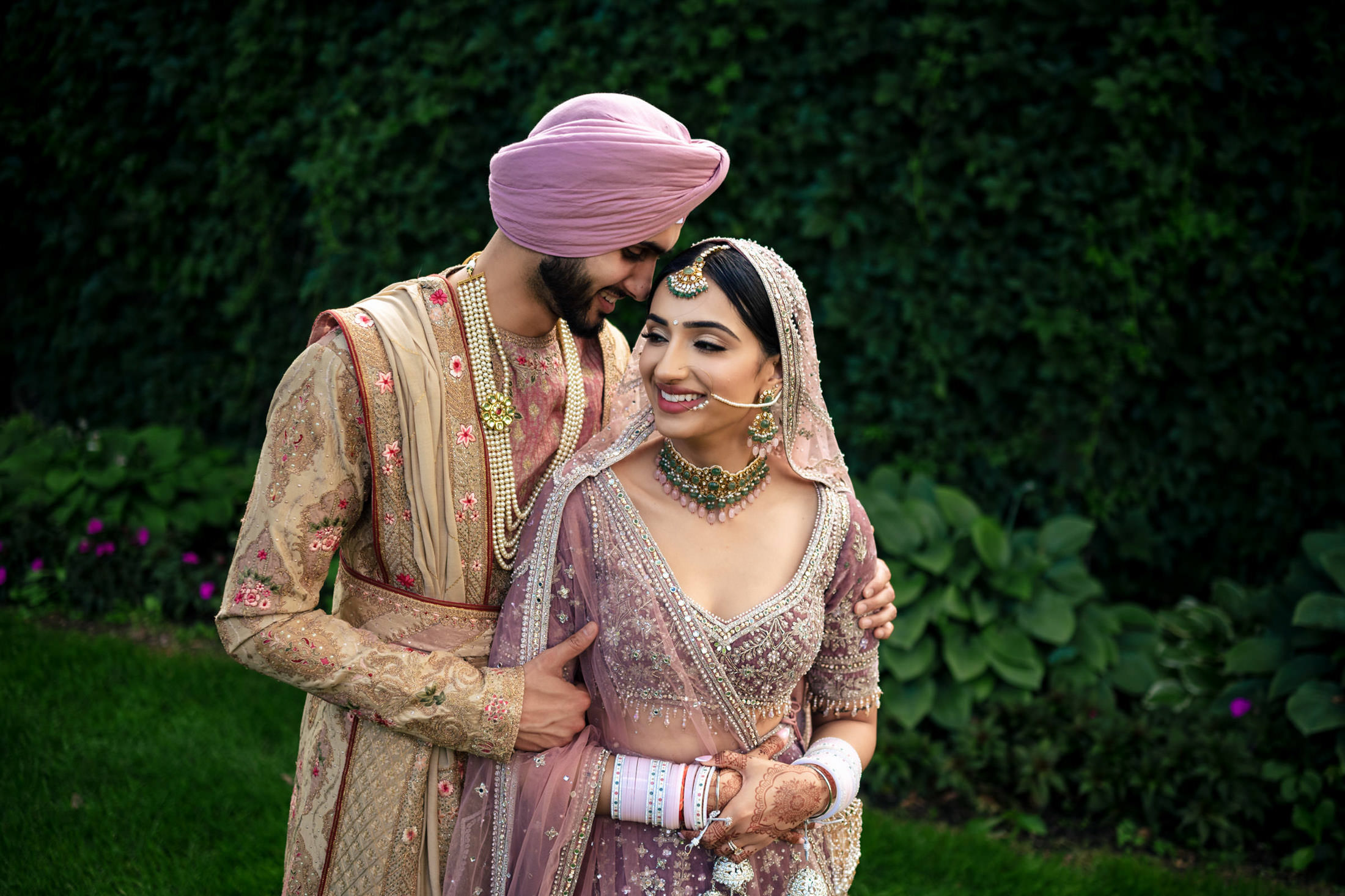 Couple in traditional Indian wedding attire, embracing in a beautiful Winnipeg garden.