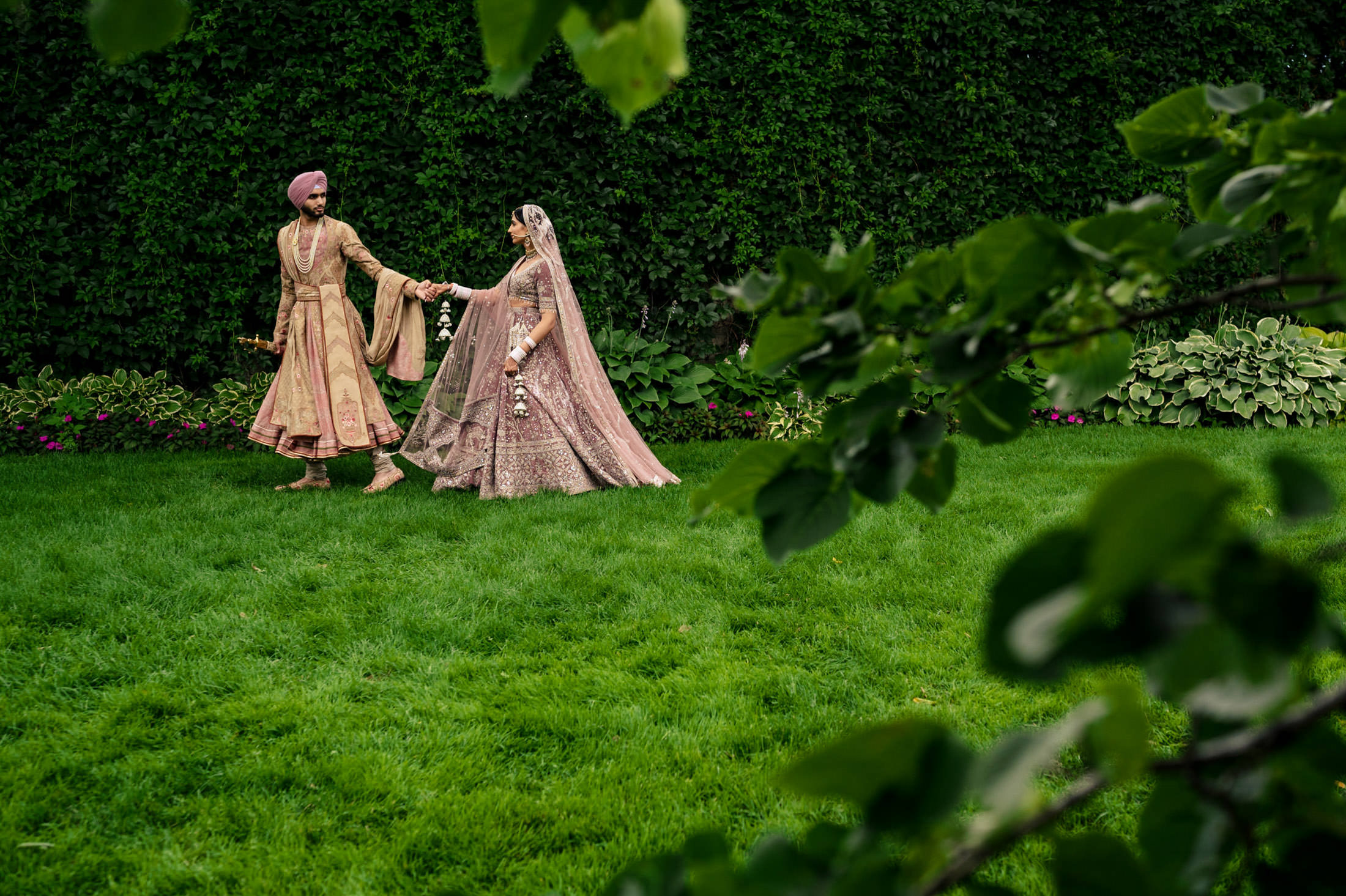 A Winnipeg wedding scene: a couple in traditional attire holding hands on a grassy lawn.