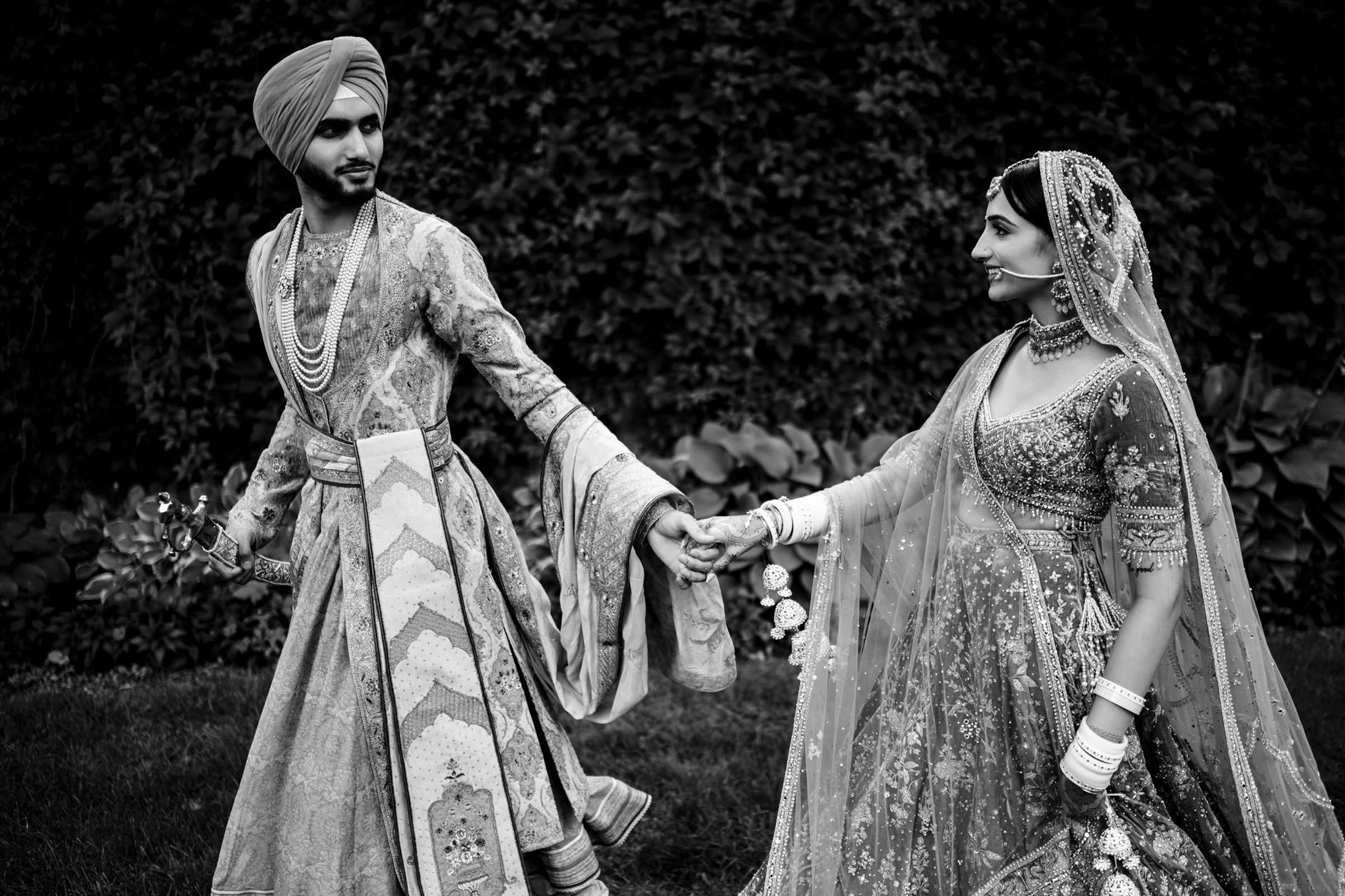 A couple in traditional attire, hand in hand, strolls through a Winnipeg wedding garden.