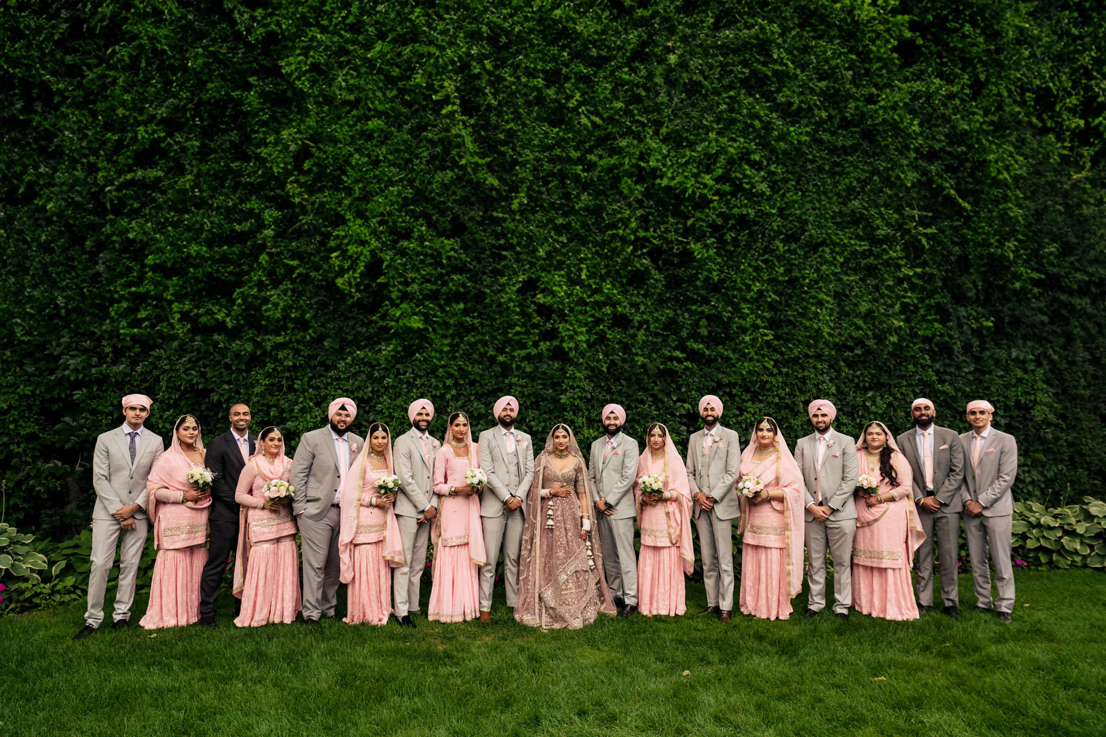 Winnipeg wedding party in pink and grey poses before a lush, ivy-covered wall.