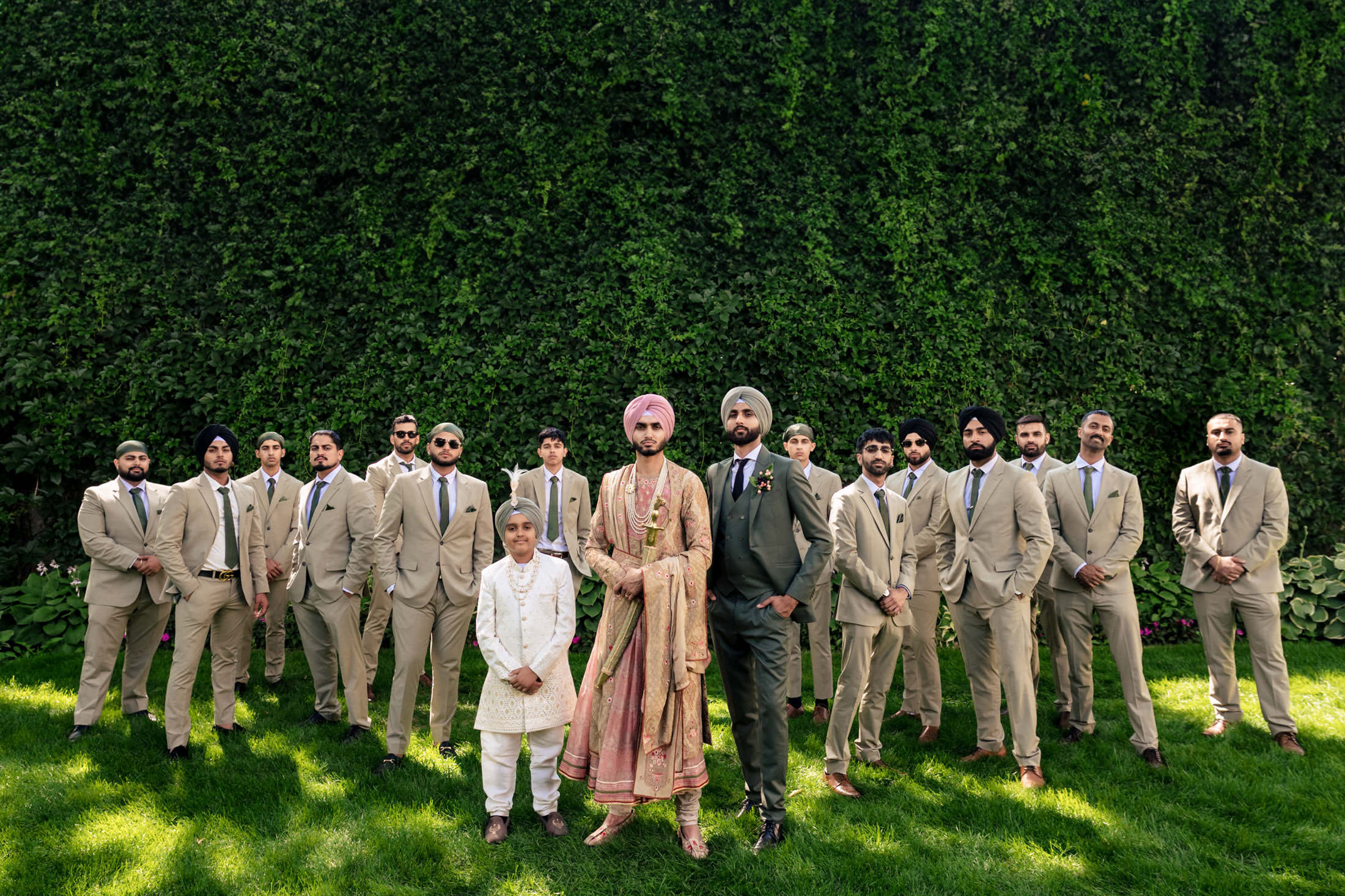 A groom and his groomsmen pose in formal attire at a Winnipeg wedding against a lush green wall.