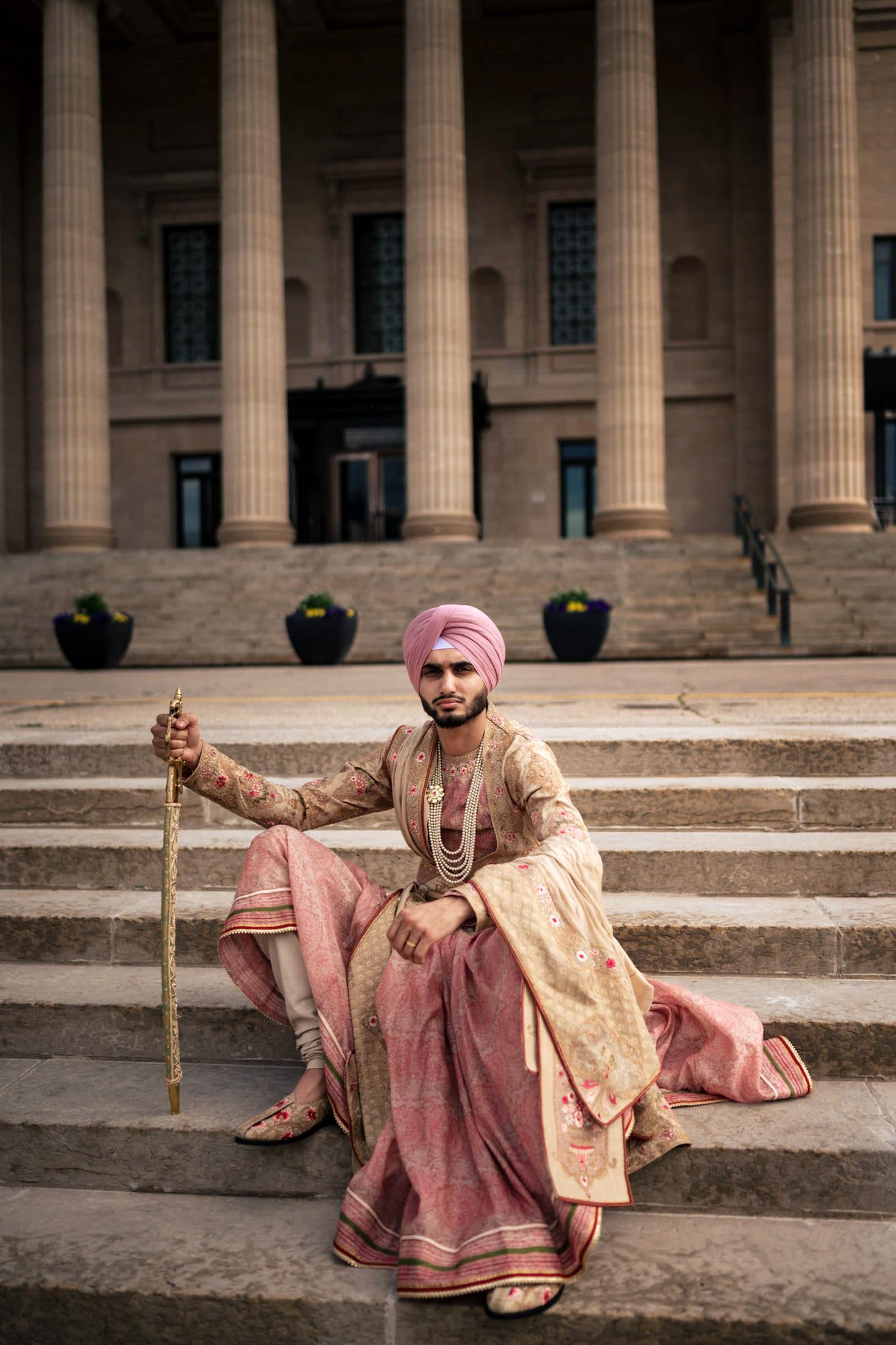 Man in traditional attire sits on steps with a sword, before Winnipeg wedding hall columns.