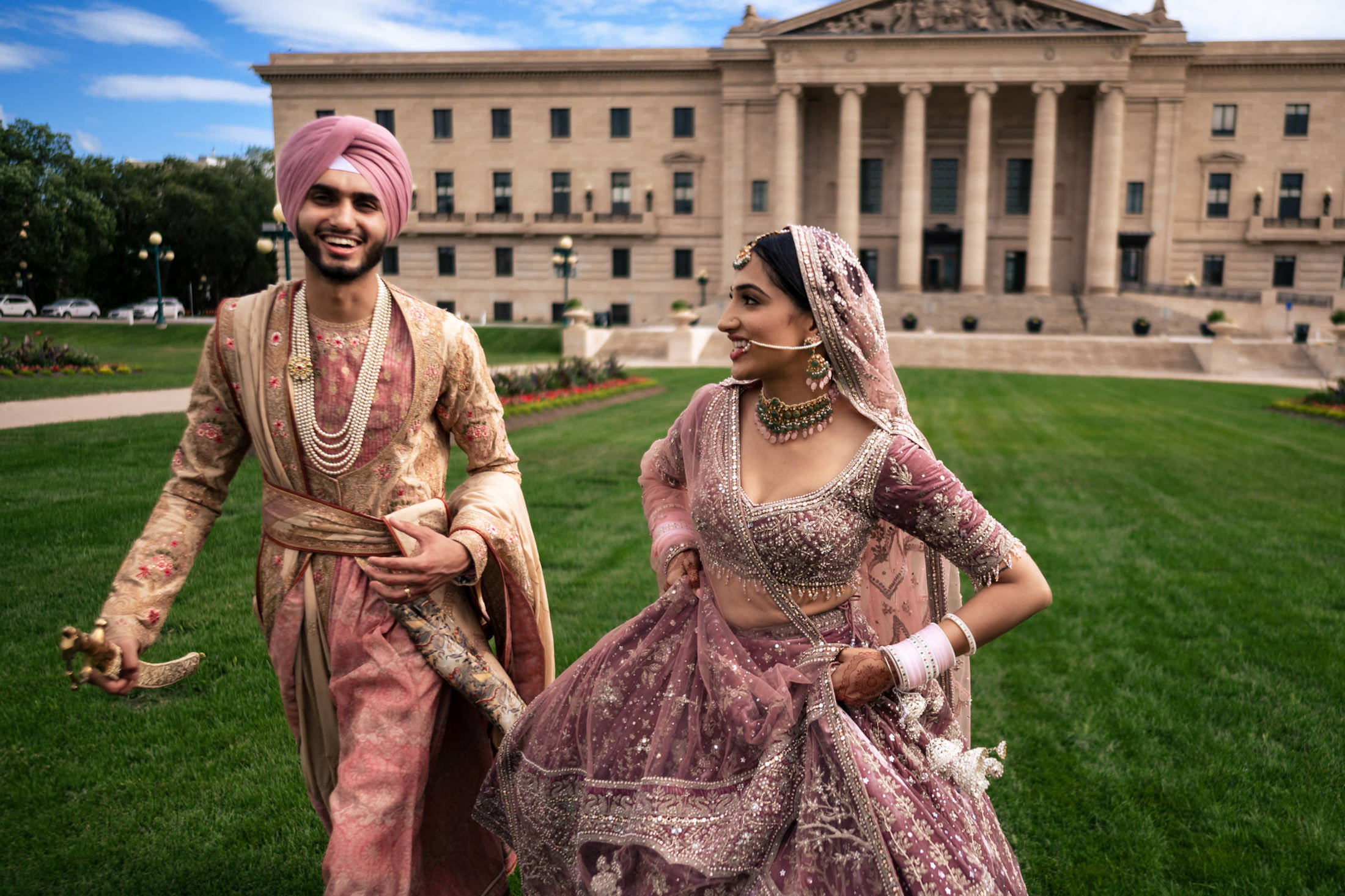 Couple in traditional attire joyfully walking at a historic Winnipeg wedding venue.