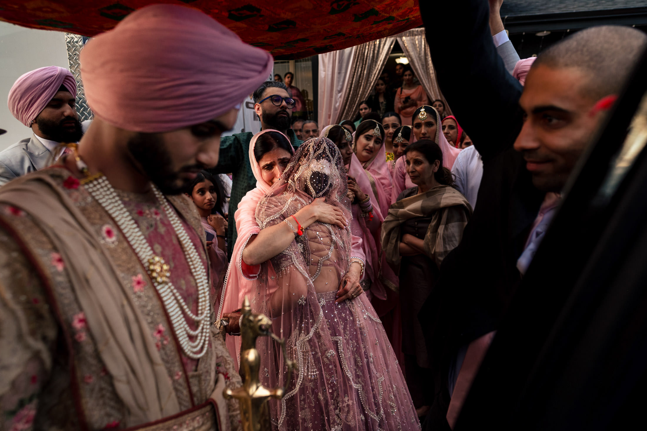 At a Winnipeg wedding, a bride in pink hugs a woman amid guests in traditional attire.