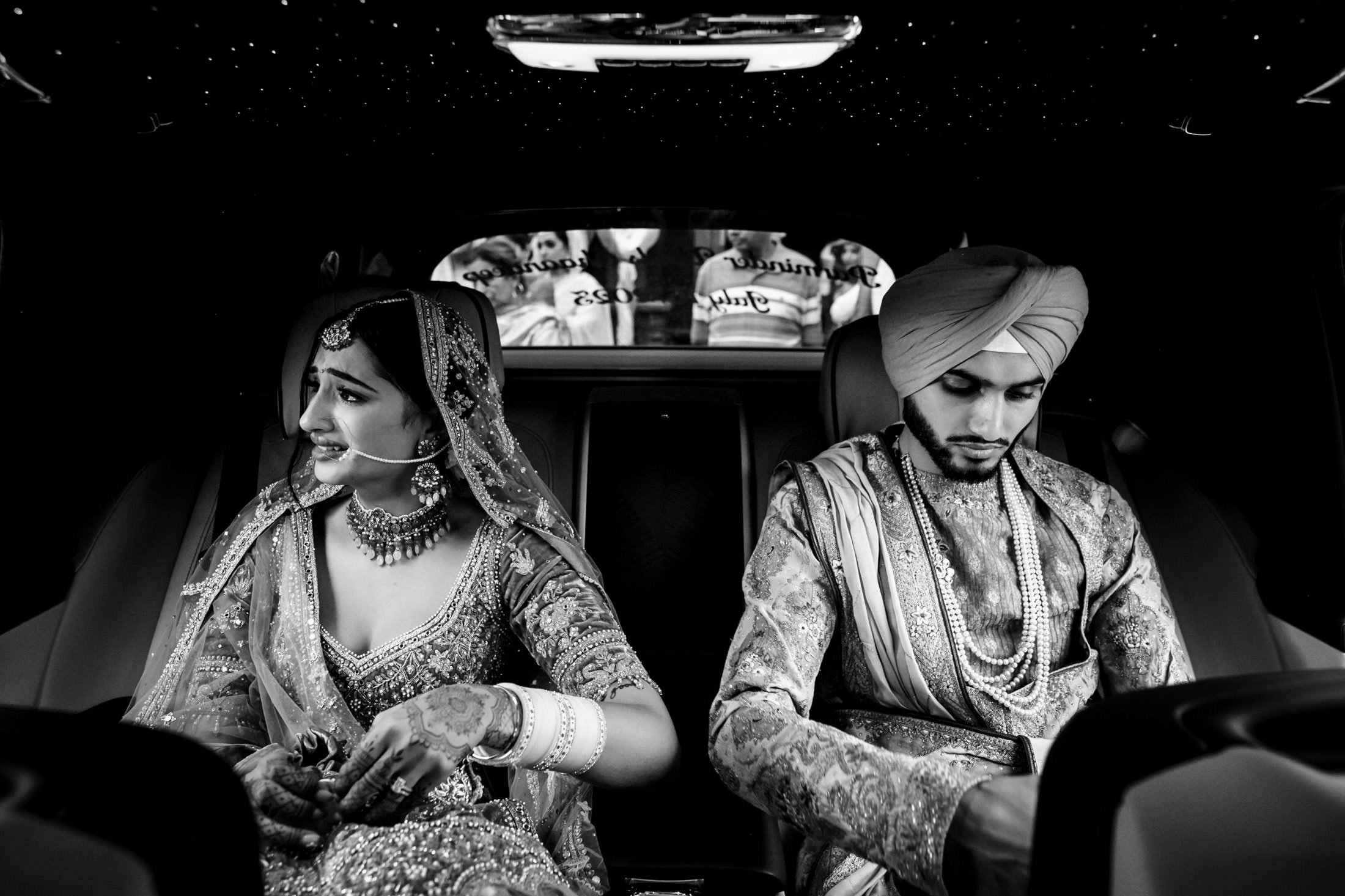 Bride and groom in traditional attire, seated in a car at a Winnipeg wedding, gaze opposite ways.