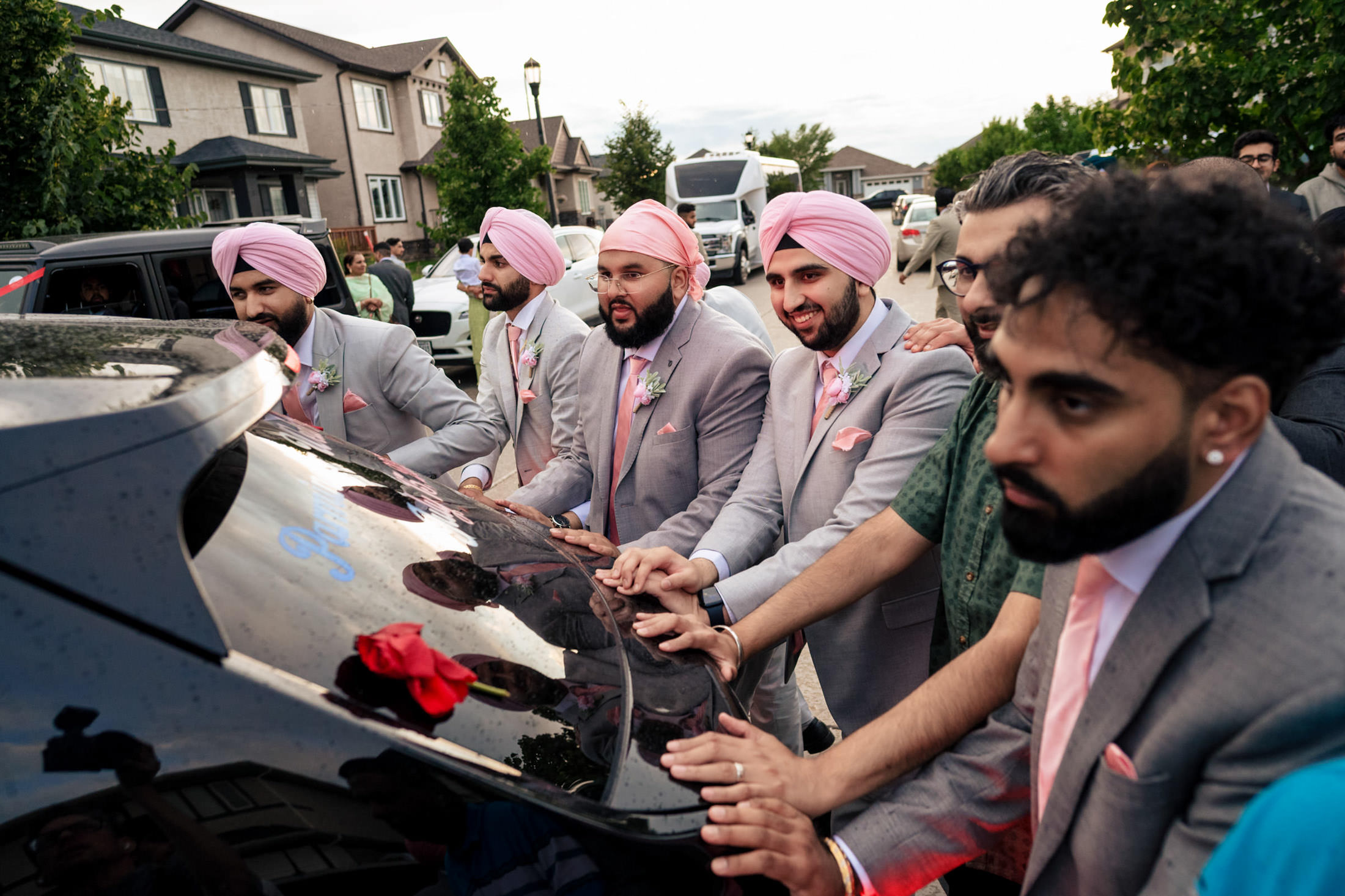 Men in pink turbans and gray suits admire a car at a Winnipeg wedding gathering.