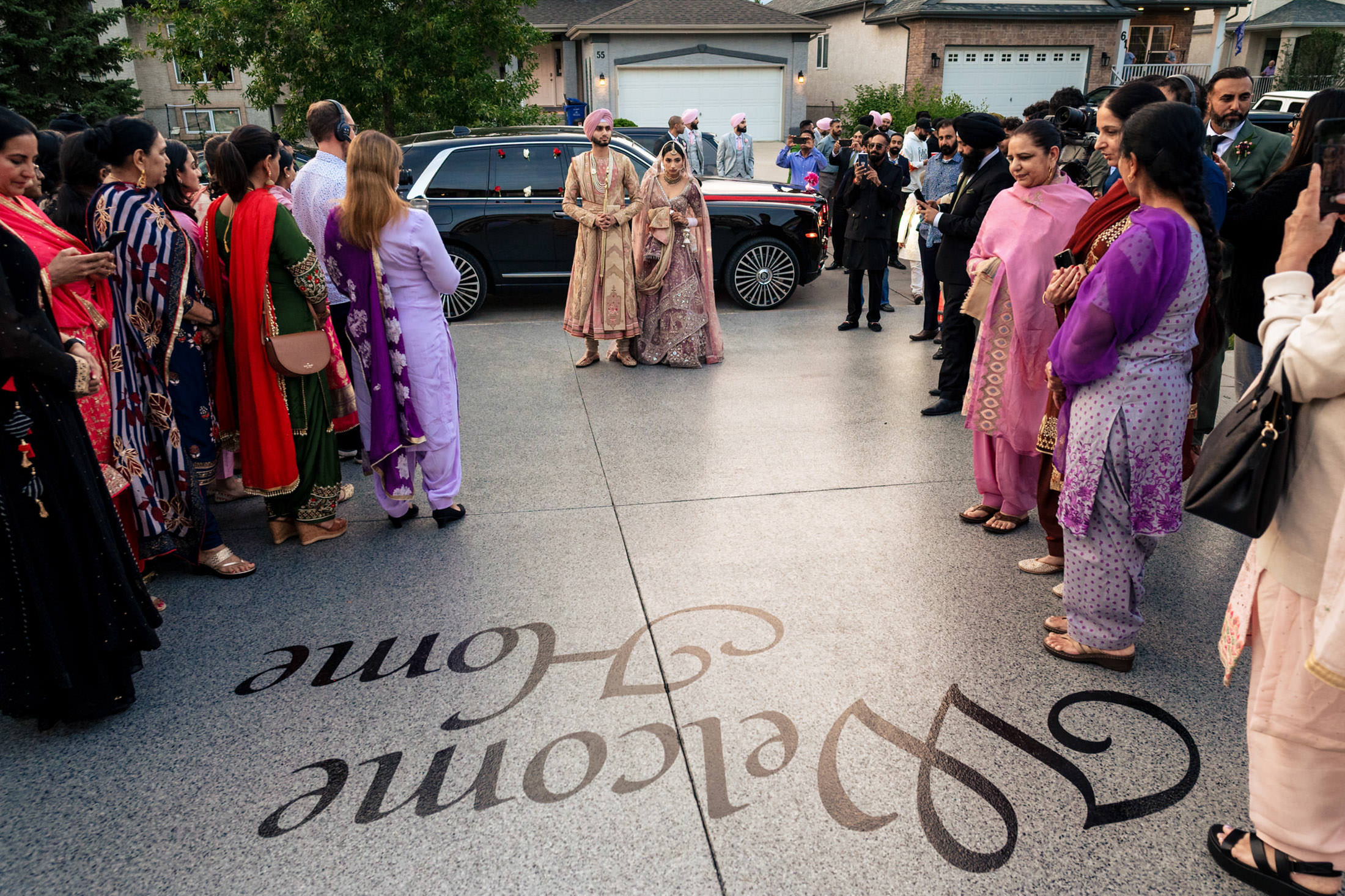 A couple in traditional attire is welcomed at a Winnipeg wedding with "Welcome Home" on the ground.