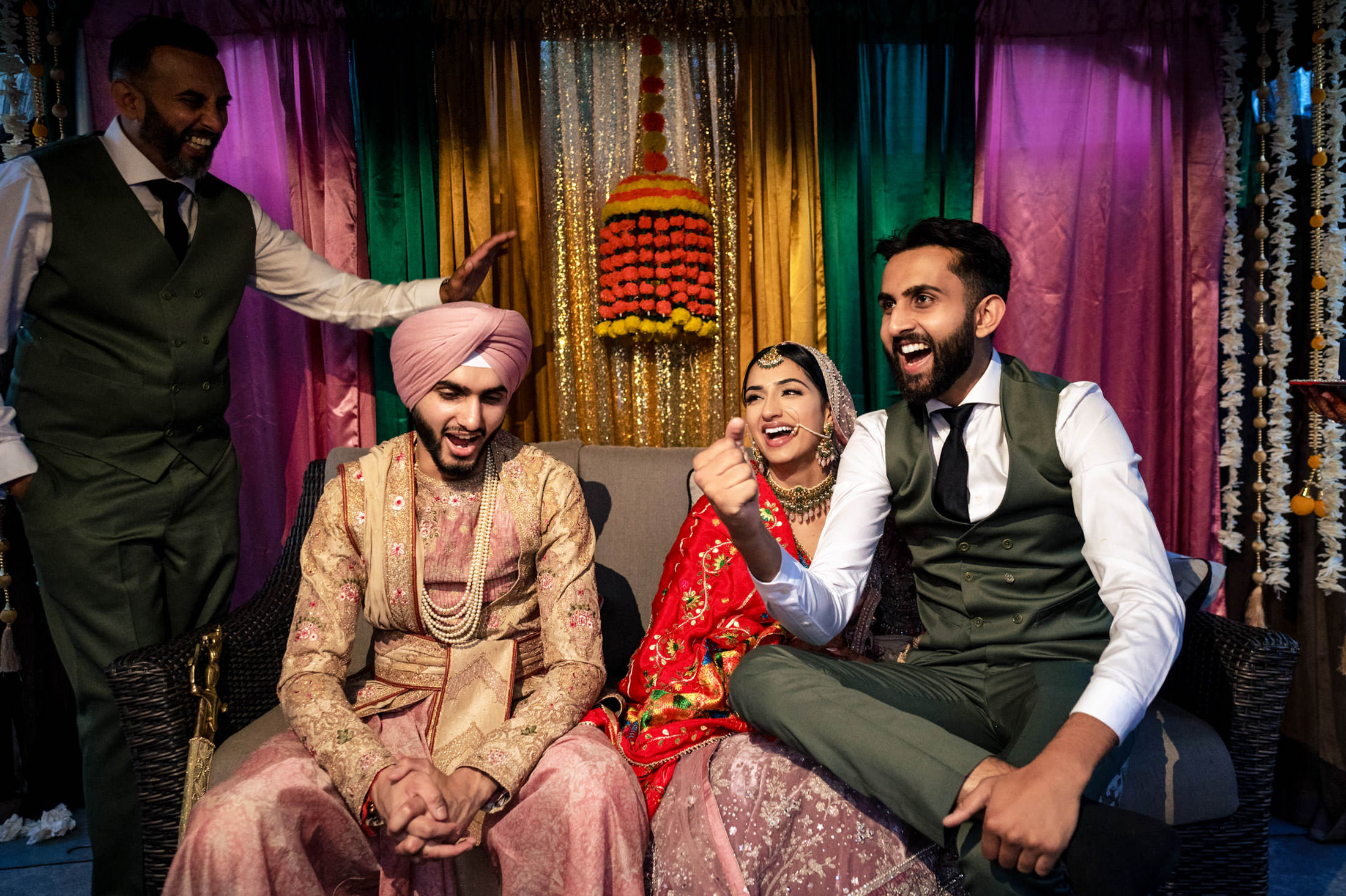Four people at a Winnipeg wedding, smiling and laughing in colorful traditional Indian outfits.