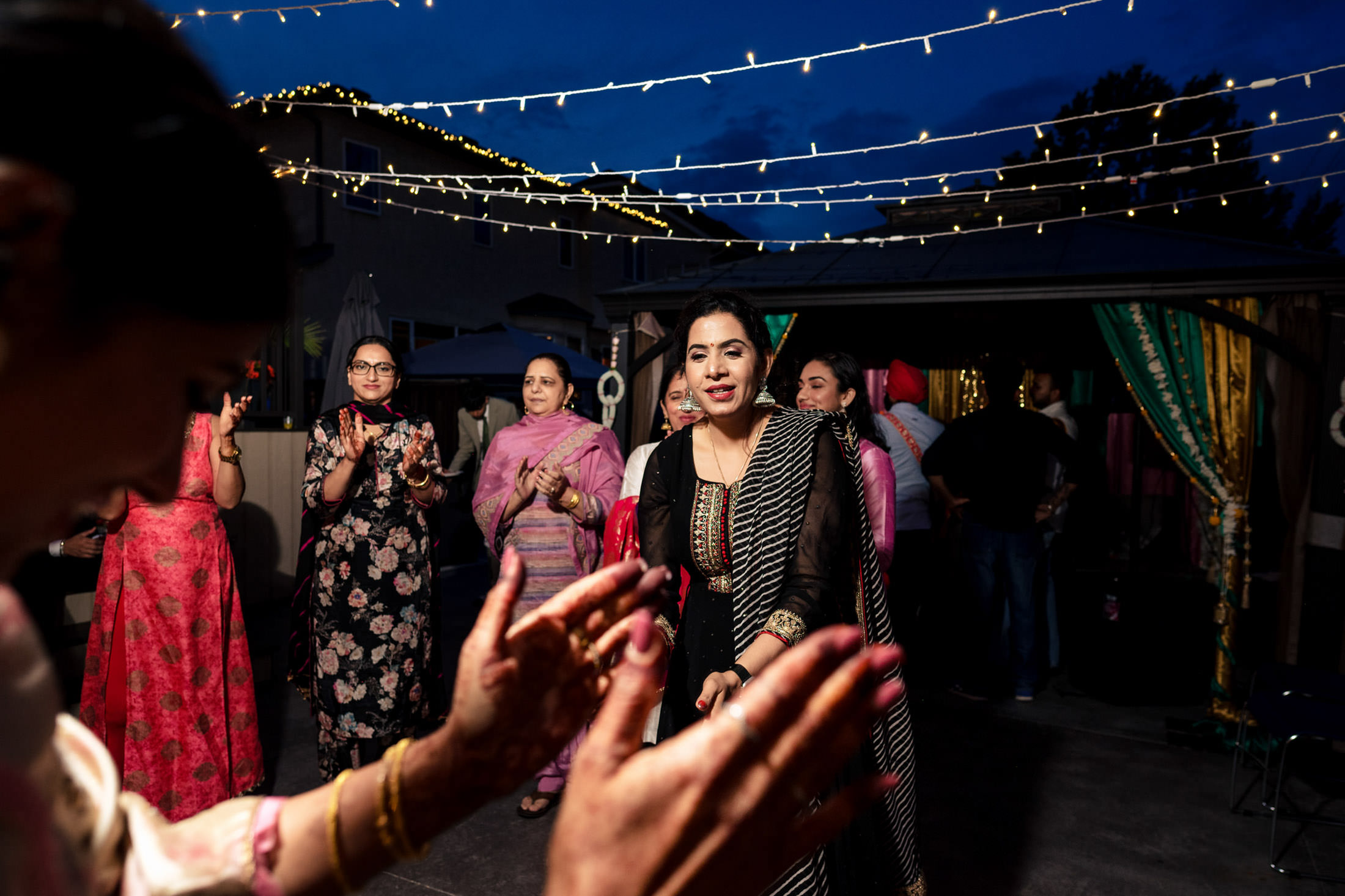 Women dancing and clapping at a Winnipeg wedding beneath twinkling string lights.