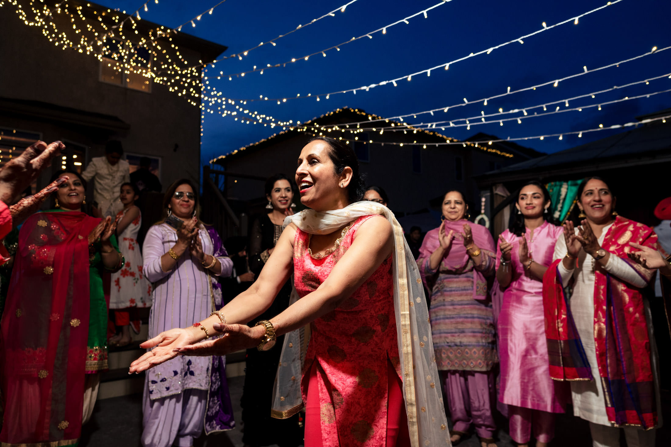 Woman dancing at a Winnipeg wedding, guests clapping with string lights overhead.