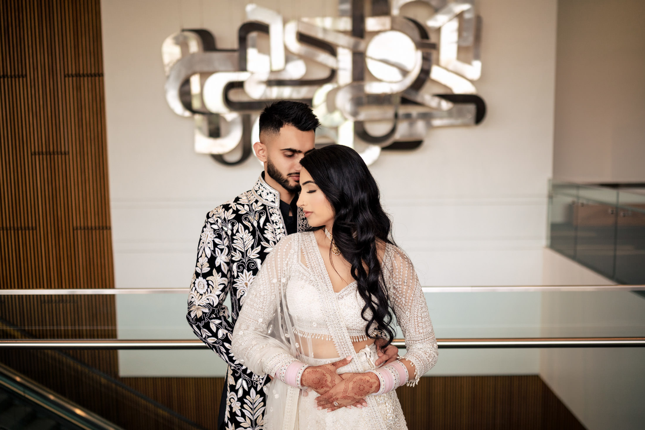 Couple in elegant attire embrace in modern Winnipeg setting with abstract wall art.