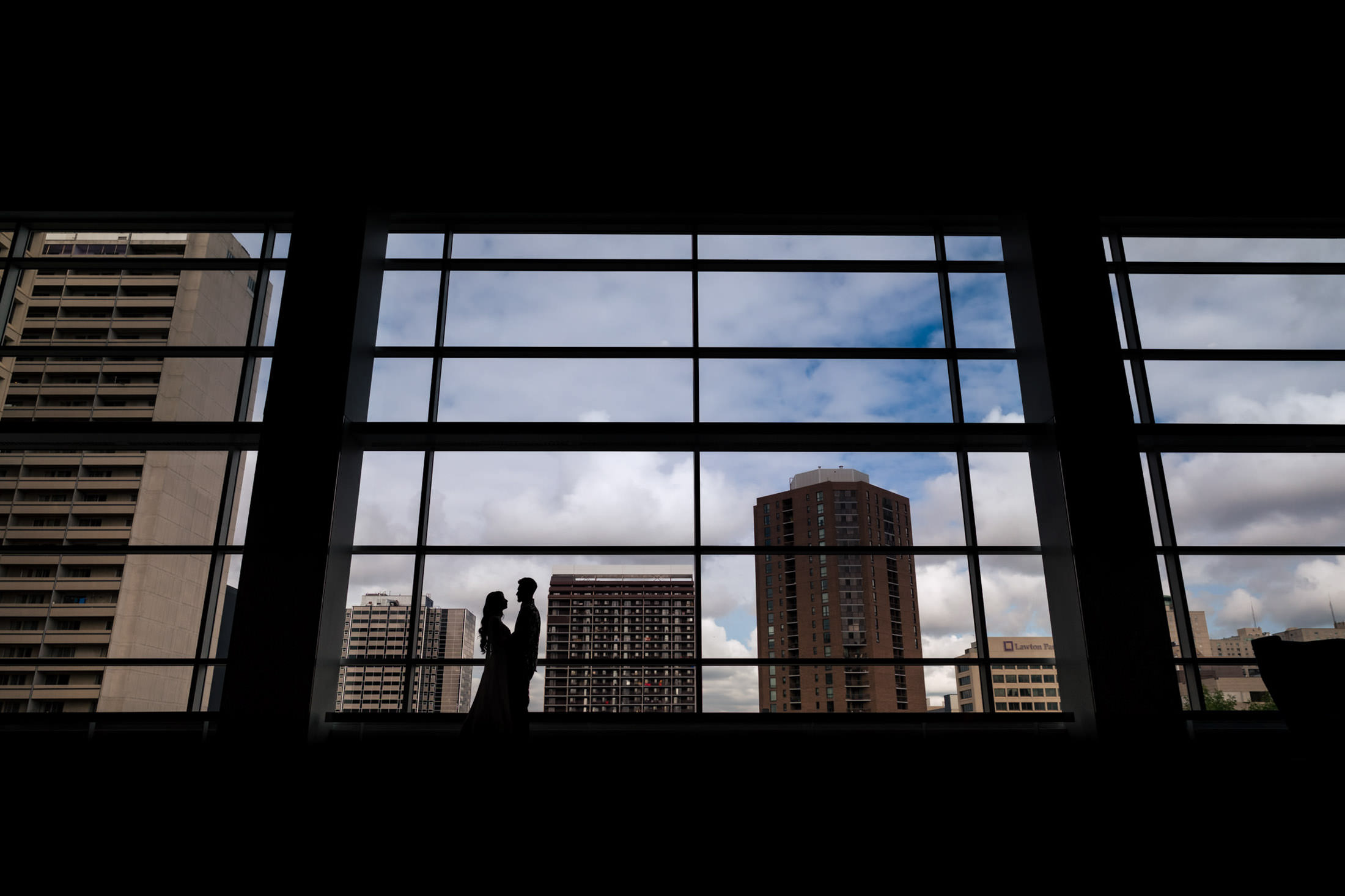 Silhouetted couple by a large window, Winnipeg wedding skyline in the background.