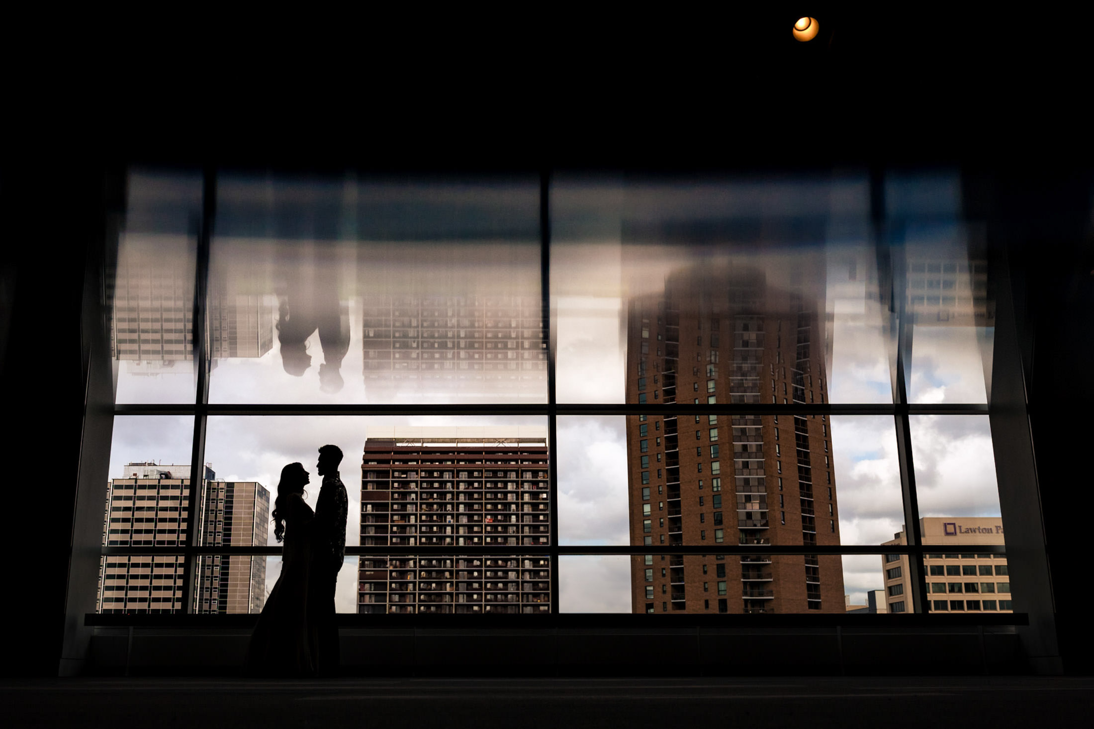 Silhouettes of a couple by large windows with Winnipeg buildings reflected in the glass.