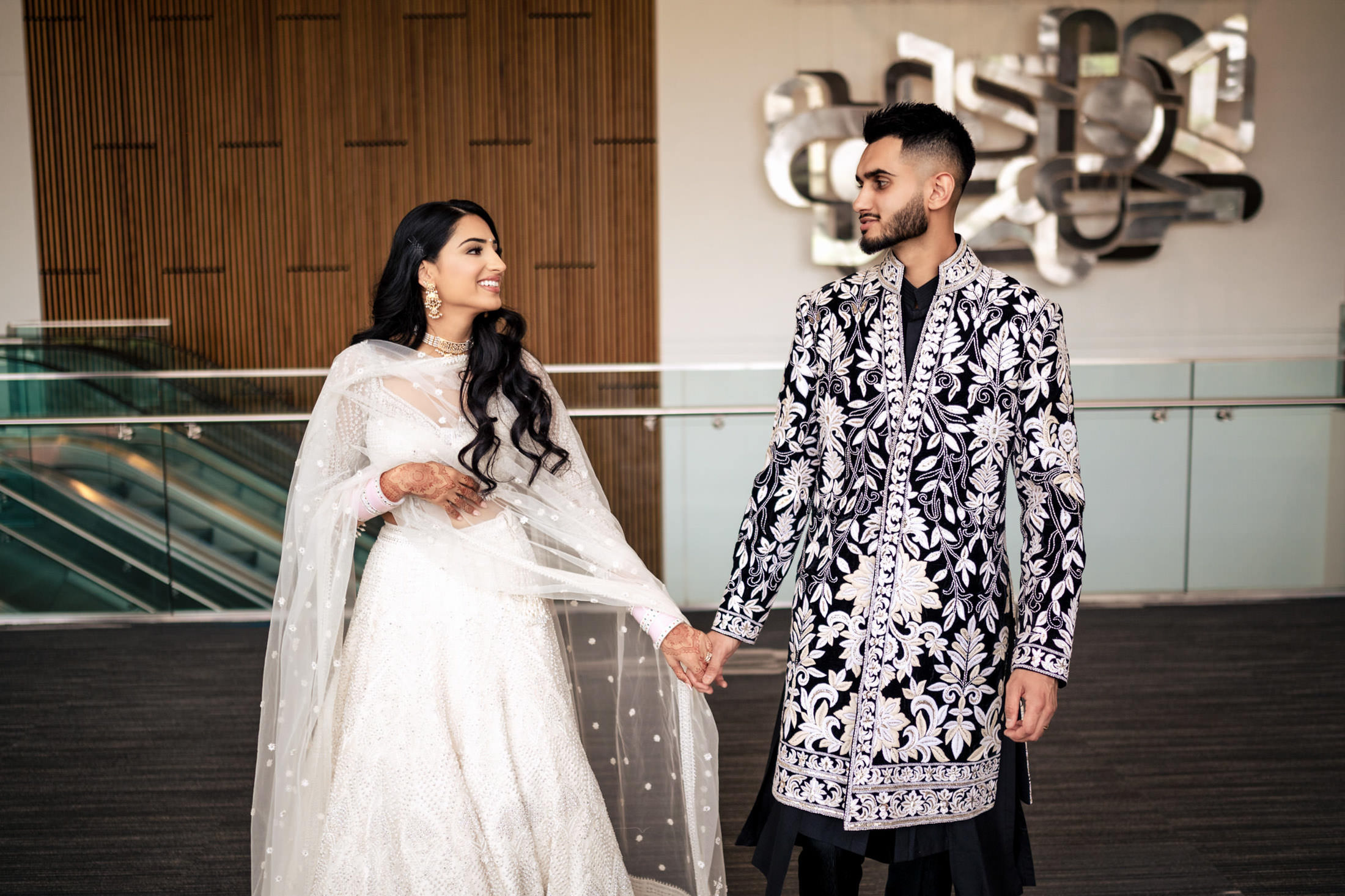 Winnipeg wedding couple in ornate black and white attire, holding hands and smiling indoors.