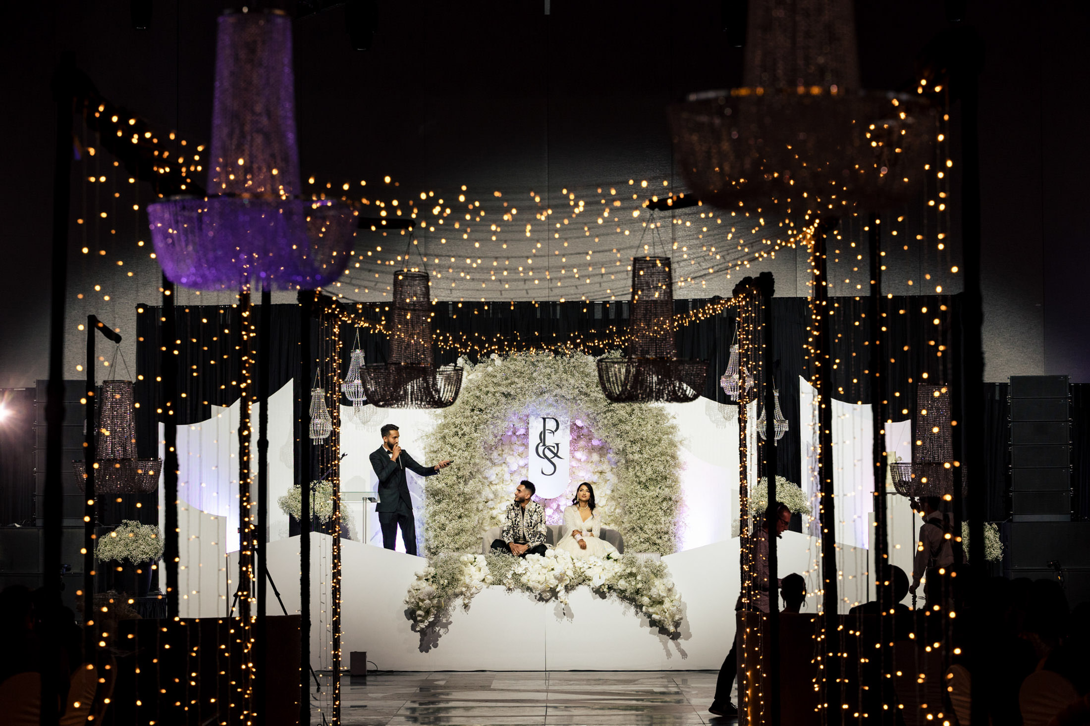 A couple shares a moment on a Winnipeg wedding stage, surrounded by lights and flowers.