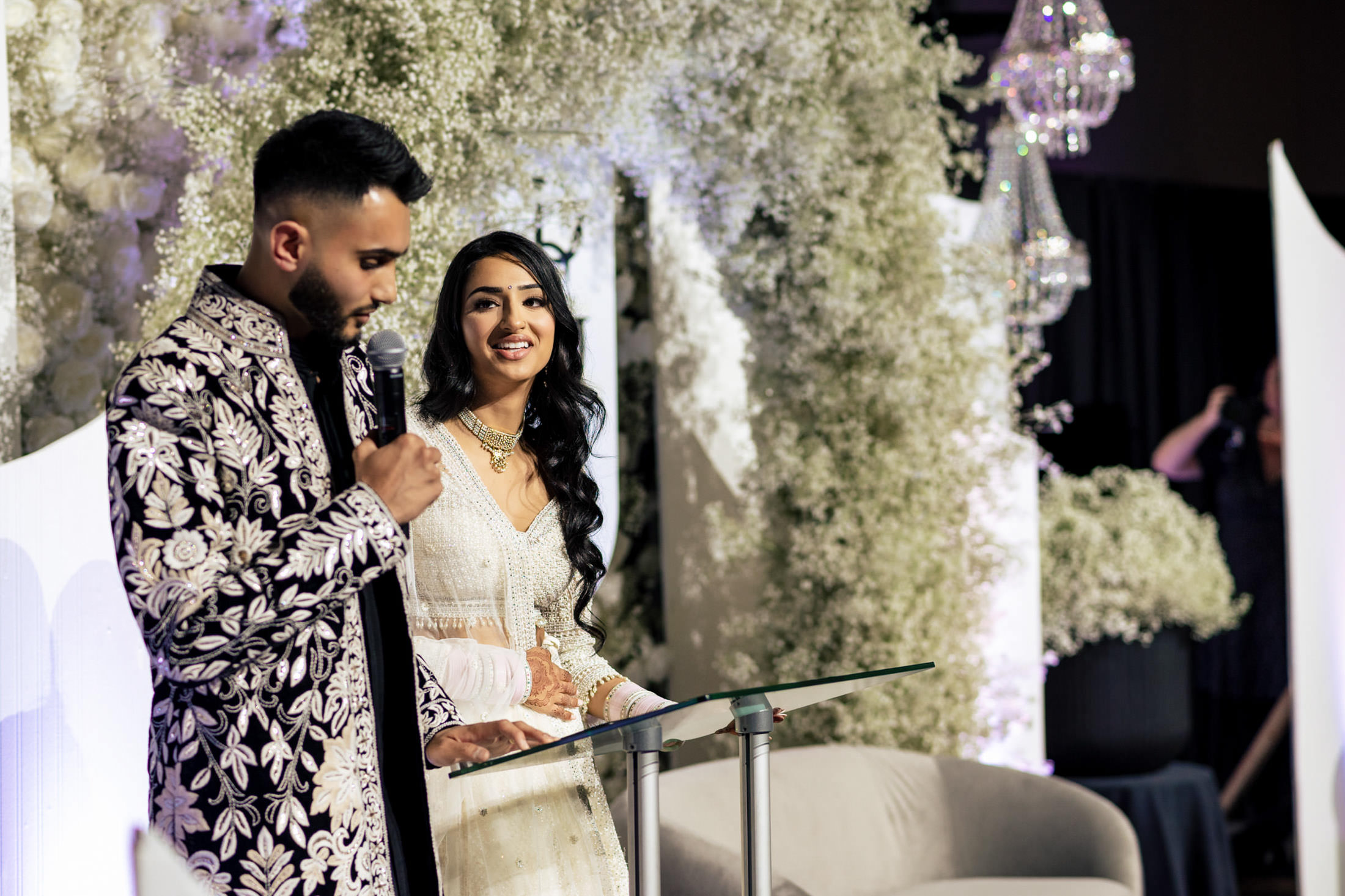 A couple speaks at a lectern, surrounded by floral decorations at a Winnipeg wedding.