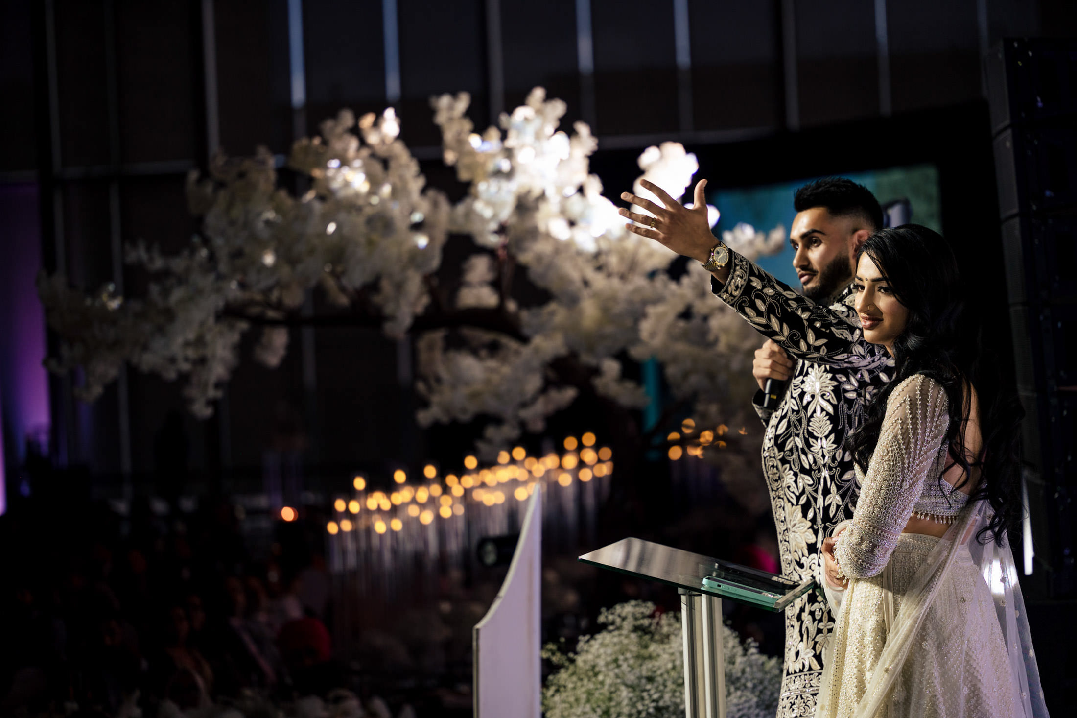 A couple in elegant attire speaks on stage at a Winnipeg wedding before a seated audience.